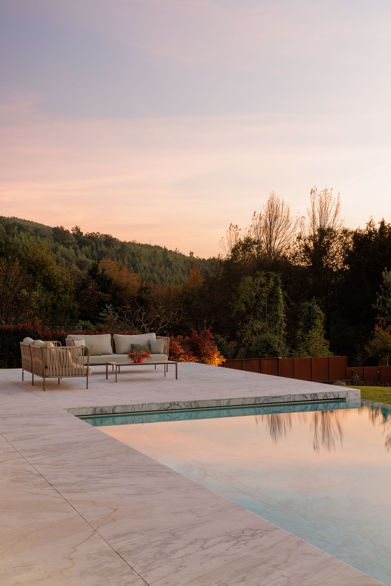 Exterior: Vista da casa com piscina infinita, alpendre e sala de estar com lareira ao entardecer. — Casa D arquitetura L2C Arquitetura em Braga