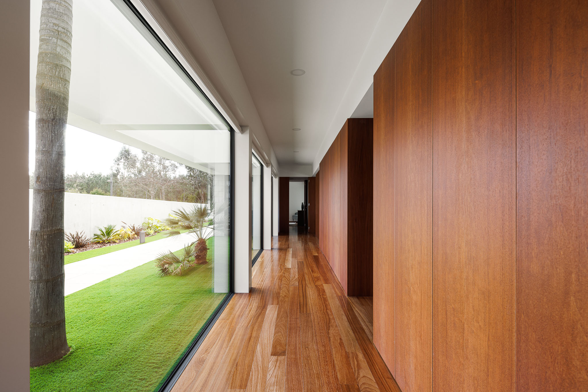 Corredor: Longo corredor com pavimento em madeira e armários embutidos. Vista para o jardim. — Casa R.V. arquitetura Atelier d´Arquitectura Lopes da Costa em Ovar