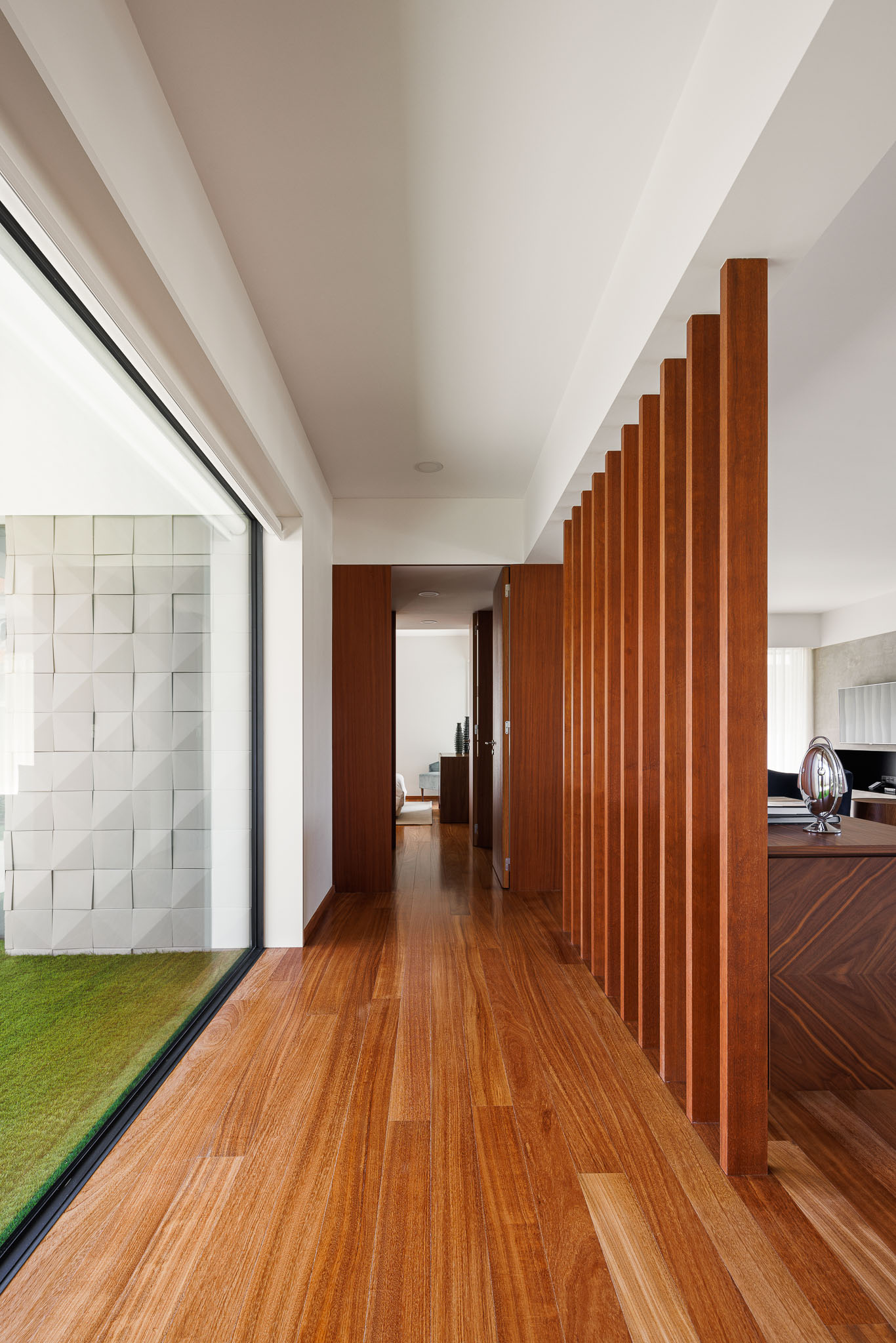 Corredor: Pavimento em madeira, divisória vertical em madeira e vista para o jardim com revestimento texturado. — Casa R.V. arquitetura Atelier d´Arquitectura Lopes da Costa em Ovar