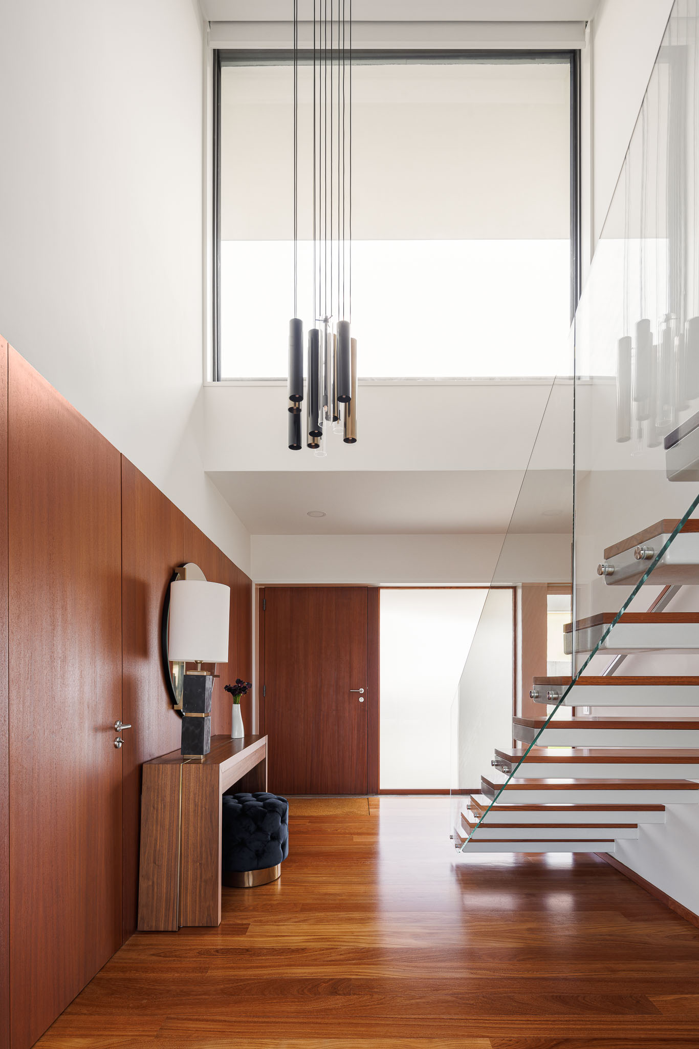 Hall de entrada: Escadas flutuantes em madeira e vidro, candeeiro suspenso e consola em madeira. — Casa R.V. arquitetura Atelier d´Arquitectura Lopes da Costa em Ovar