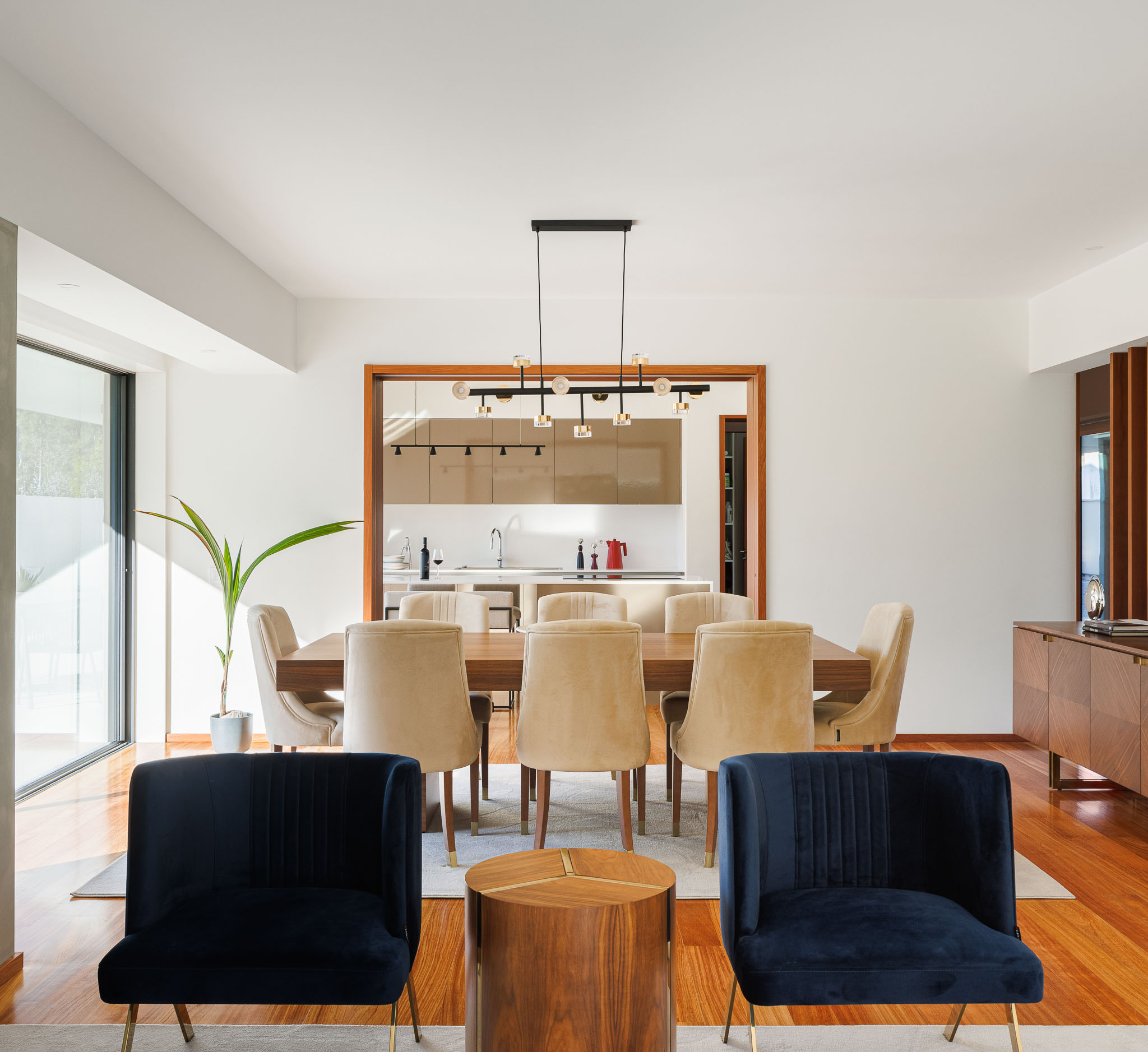 Sala de jantar: Mesa em madeira, cadeiras em veludo, candeeiro suspenso e vista para a cozinha. — Casa R.V. arquitetura Atelier d´Arquitectura Lopes da Costa em Ovar