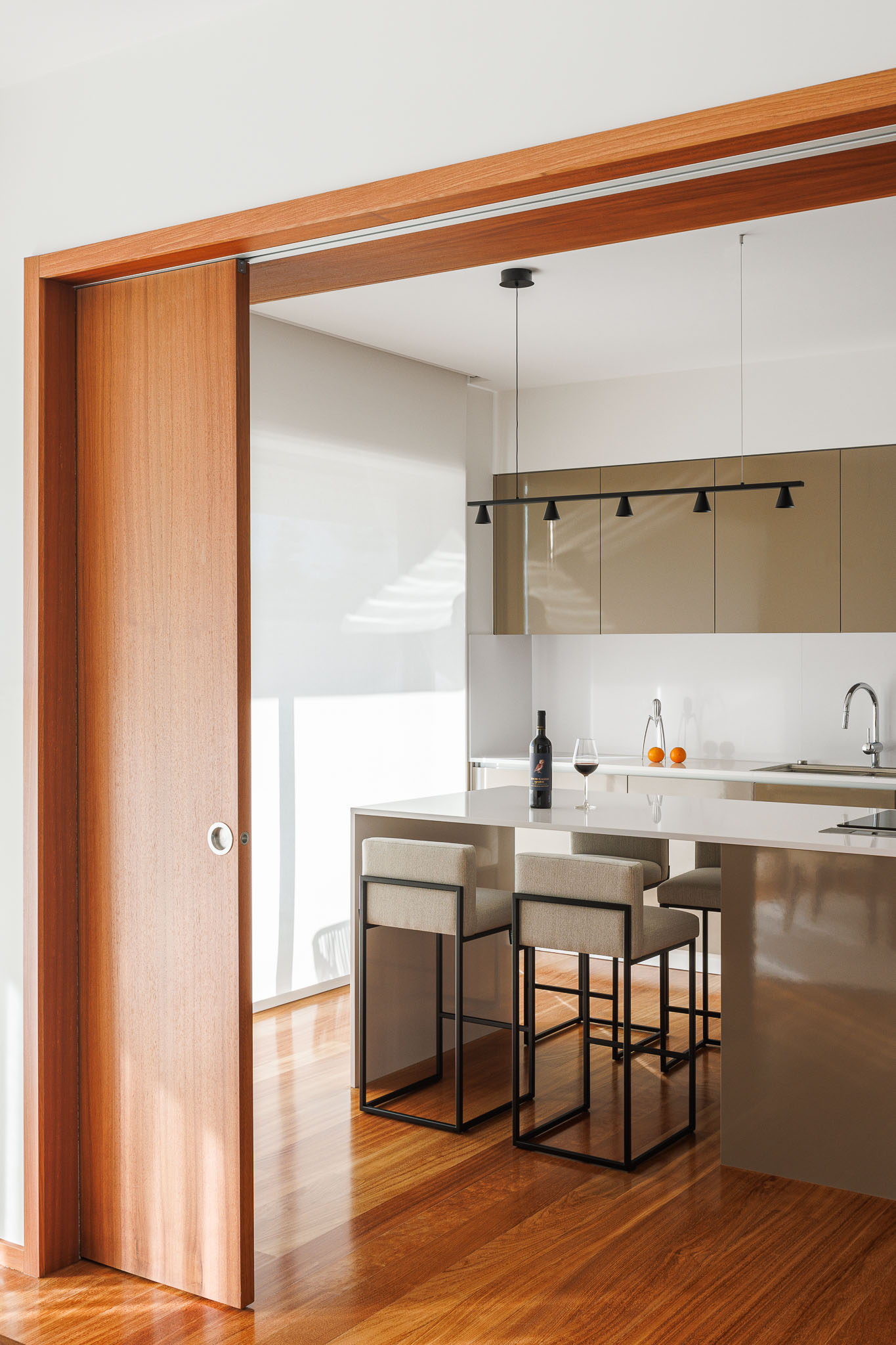 Cozinha: Porta de correr em madeira, ilha central com cadeiras altas e armários modernos. — Casa R.V. arquitetura Atelier d´Arquitectura Lopes da Costa em Ovar