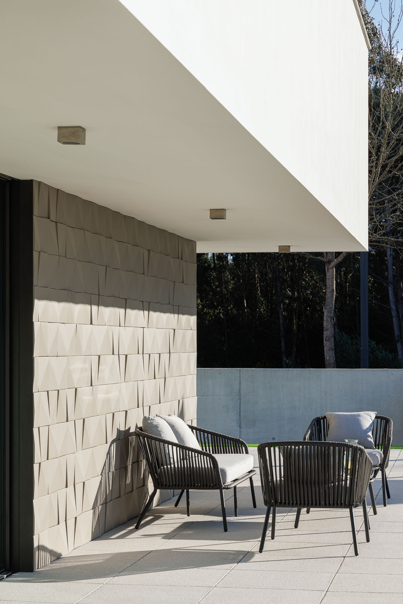 Terraço: Mobiliário de exterior em vime, pavimento em pedra e parede com revestimento texturado. — Casa R.V. arquitetura Atelier d´Arquitectura Lopes da Costa em Ovar