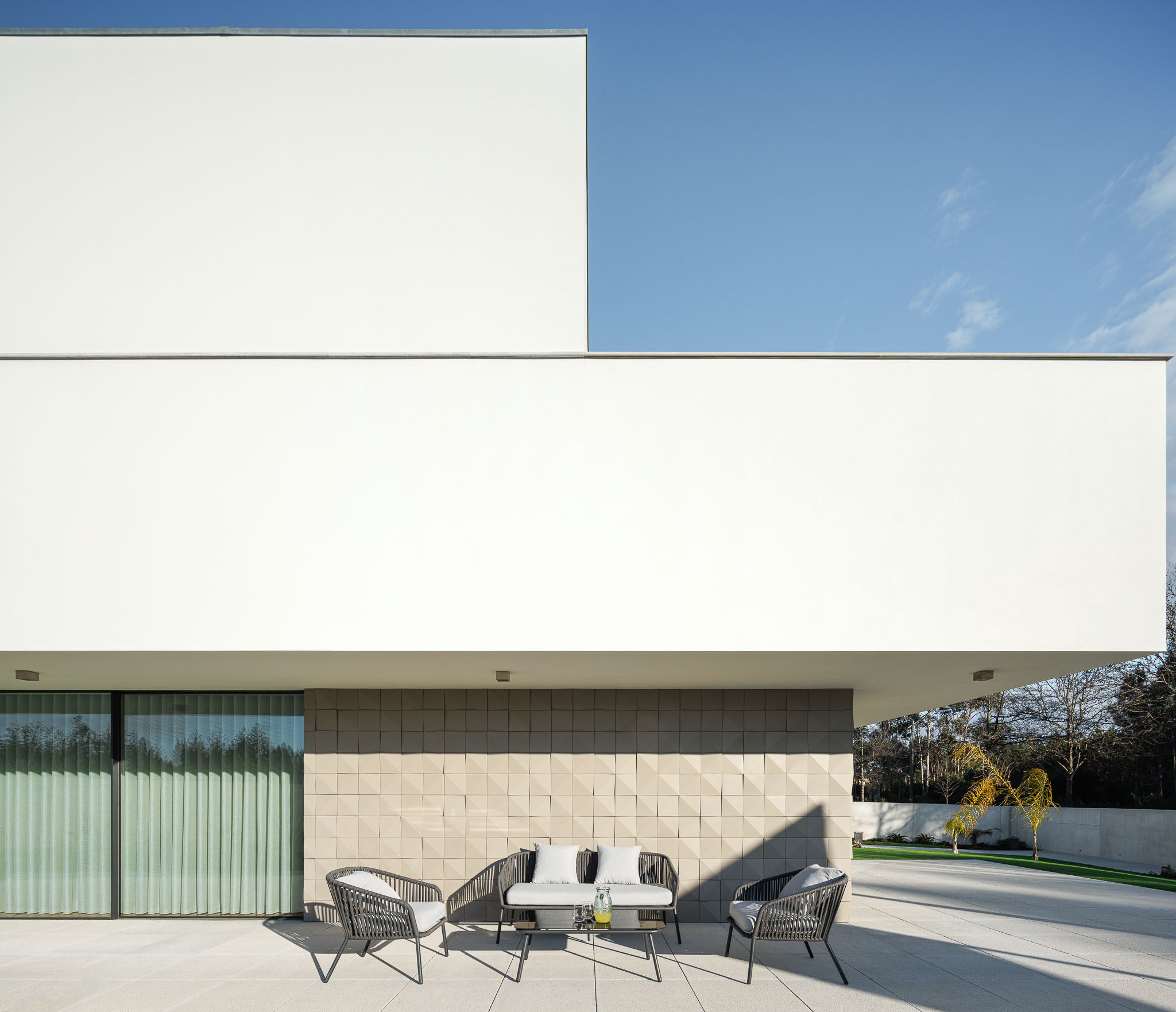 Terraço: Mobiliário de exterior em vime, pavimento em pedra e fachada branca com revestimento texturado. — Casa R.V. arquitetura Atelier d´Arquitectura Lopes da Costa em Ovar