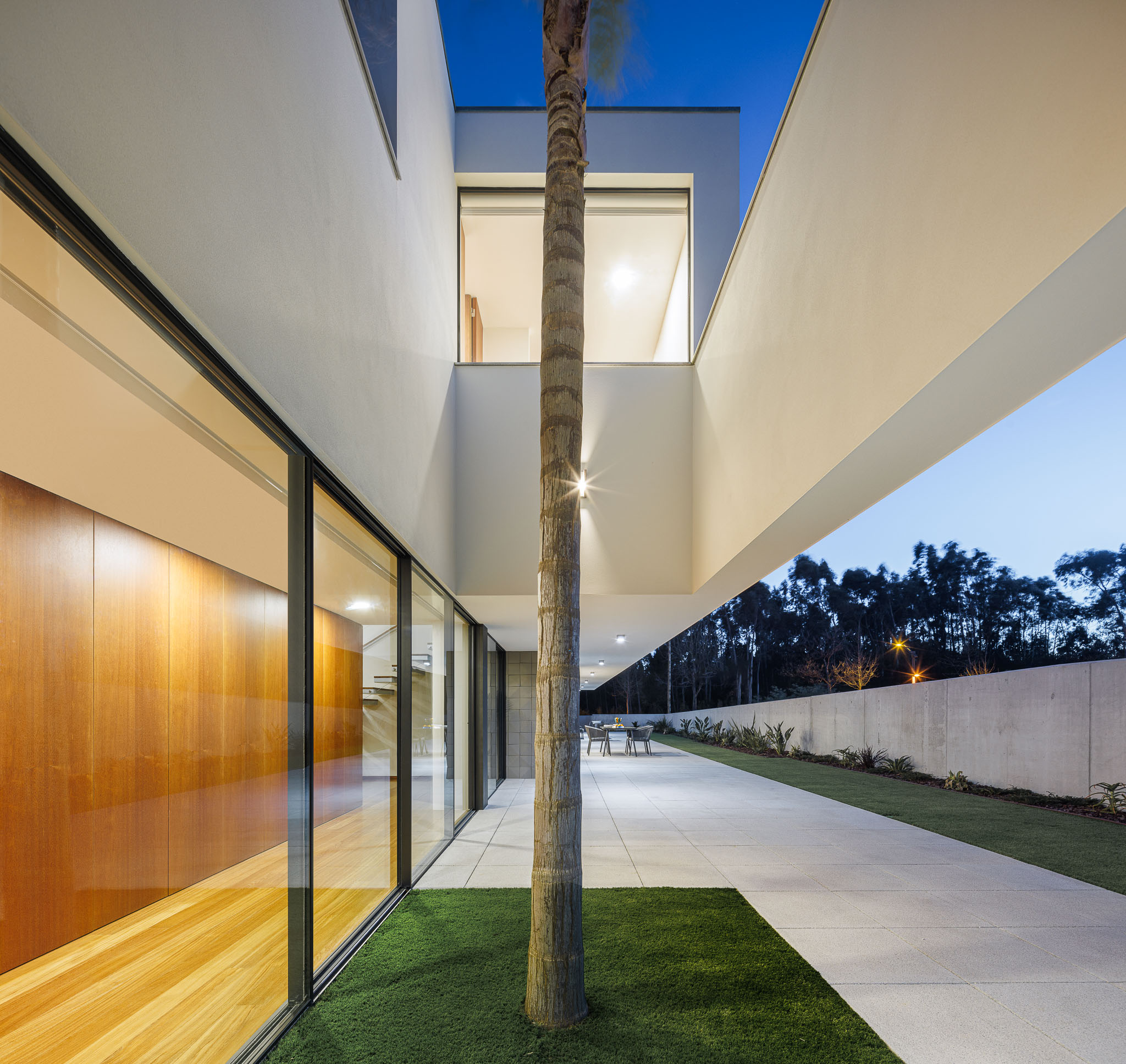 Exterior: Pátio interior da casa ao anoitecer, com árvore central e vista para o jardim. — Casa R.V. arquitetura Atelier d´Arquitectura Lopes da Costa em Ovar