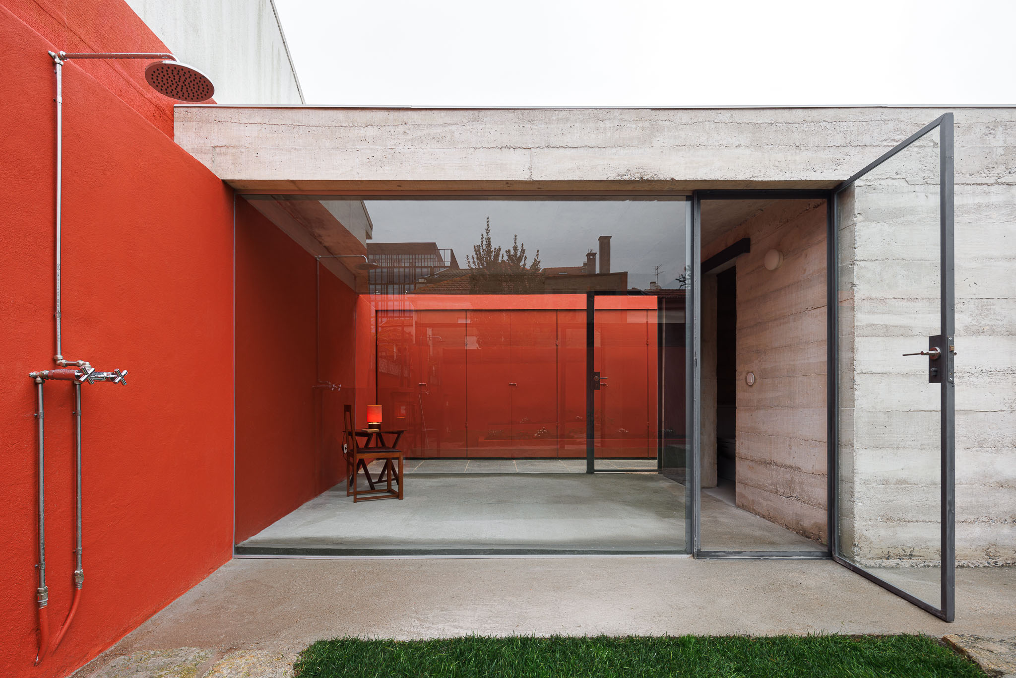 Exterior: Duche exterior, porta envidraçada para o interior, parede vermelha e estrutura em betão. — Pavilhão de jardim arquitetura José Pedro Lima Arquiteto em Porto