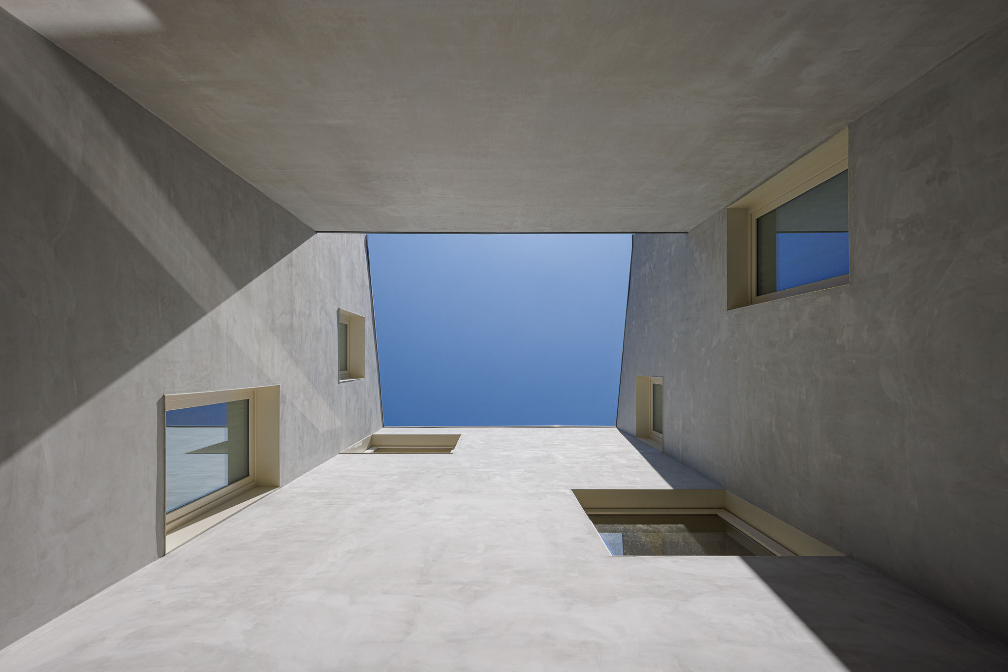 Pátio interior: Vista vertical do pátio interior com paredes em betão aparente e janelas, criando um espaço luminoso e minimalista. — Villa Theatro arquitetura arquitectos aliados em Braga