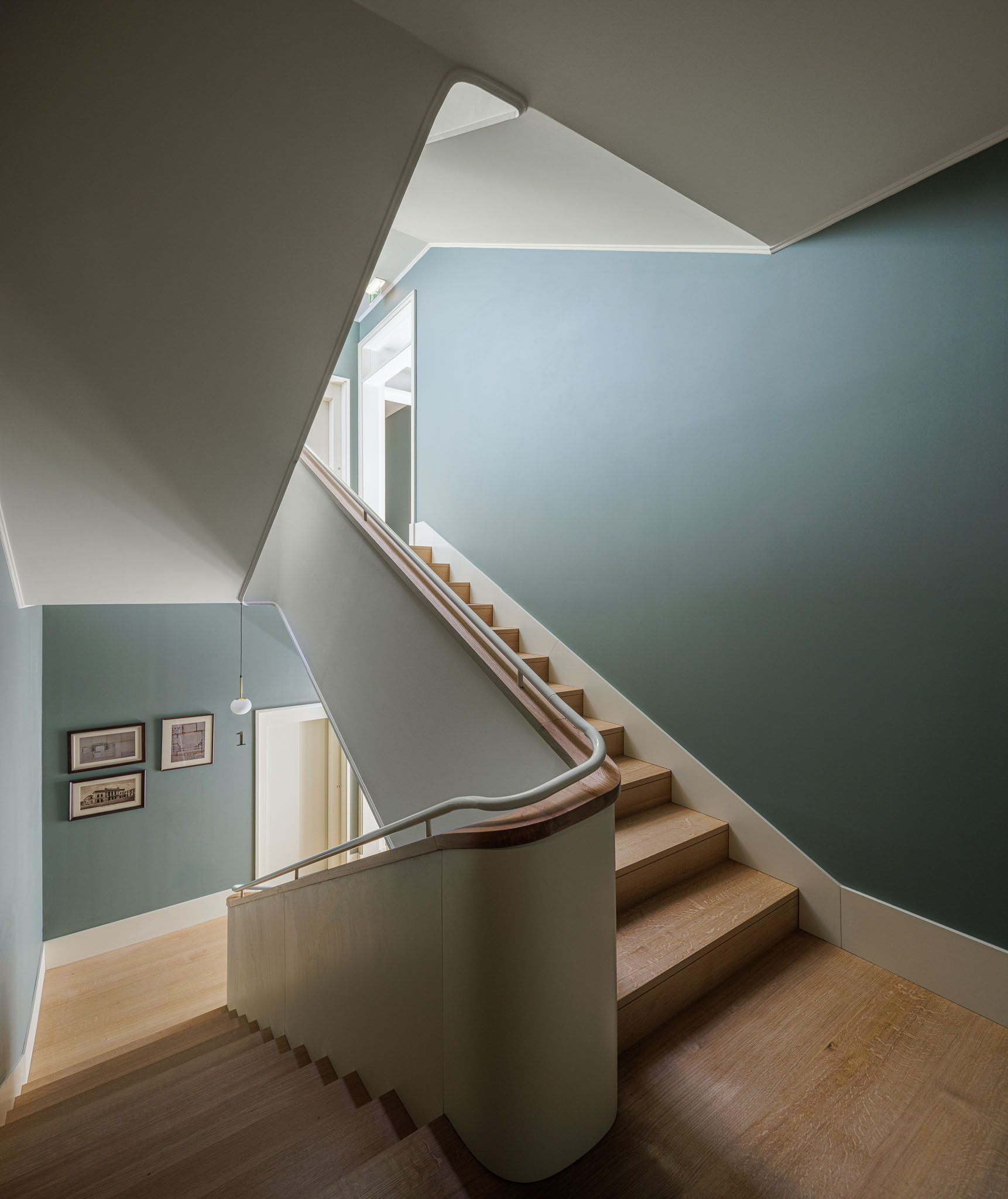 Escada: Vista da escada com degraus em madeira clara, corrimão em metal e paredes em tons de verde, com quadros decorativos. — Villa Theatro arquitetura arquitectos aliados em Braga