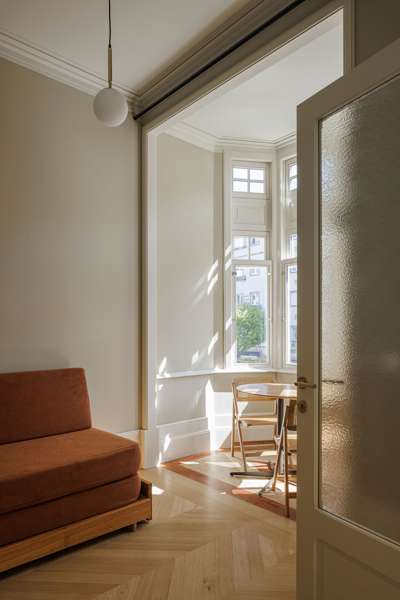 Sala de estar: Sofá laranja, mesa redonda e cadeiras em madeira, com pavimento em madeira clara e luz natural da janela. — Villa Theatro arquitetura arquitectos aliados em Braga