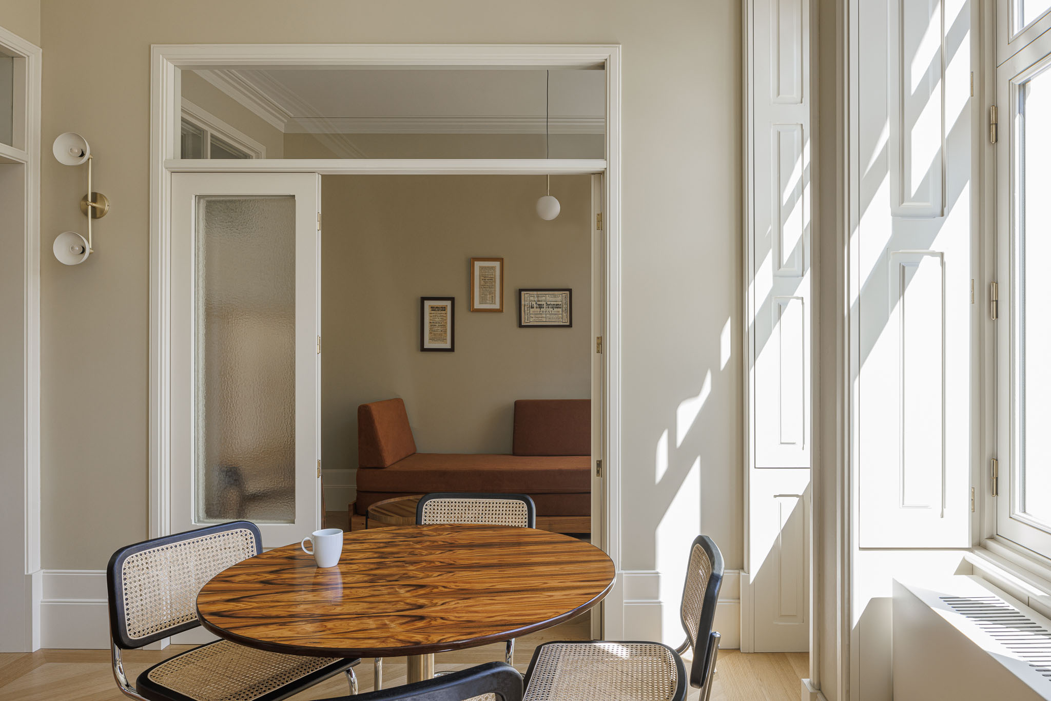 Sala de jantar: Mesa redonda em madeira escura com cadeiras de vime, sofá laranja ao fundo e candeeiro pendente. — Villa Theatro arquitetura arquitectos aliados em Braga