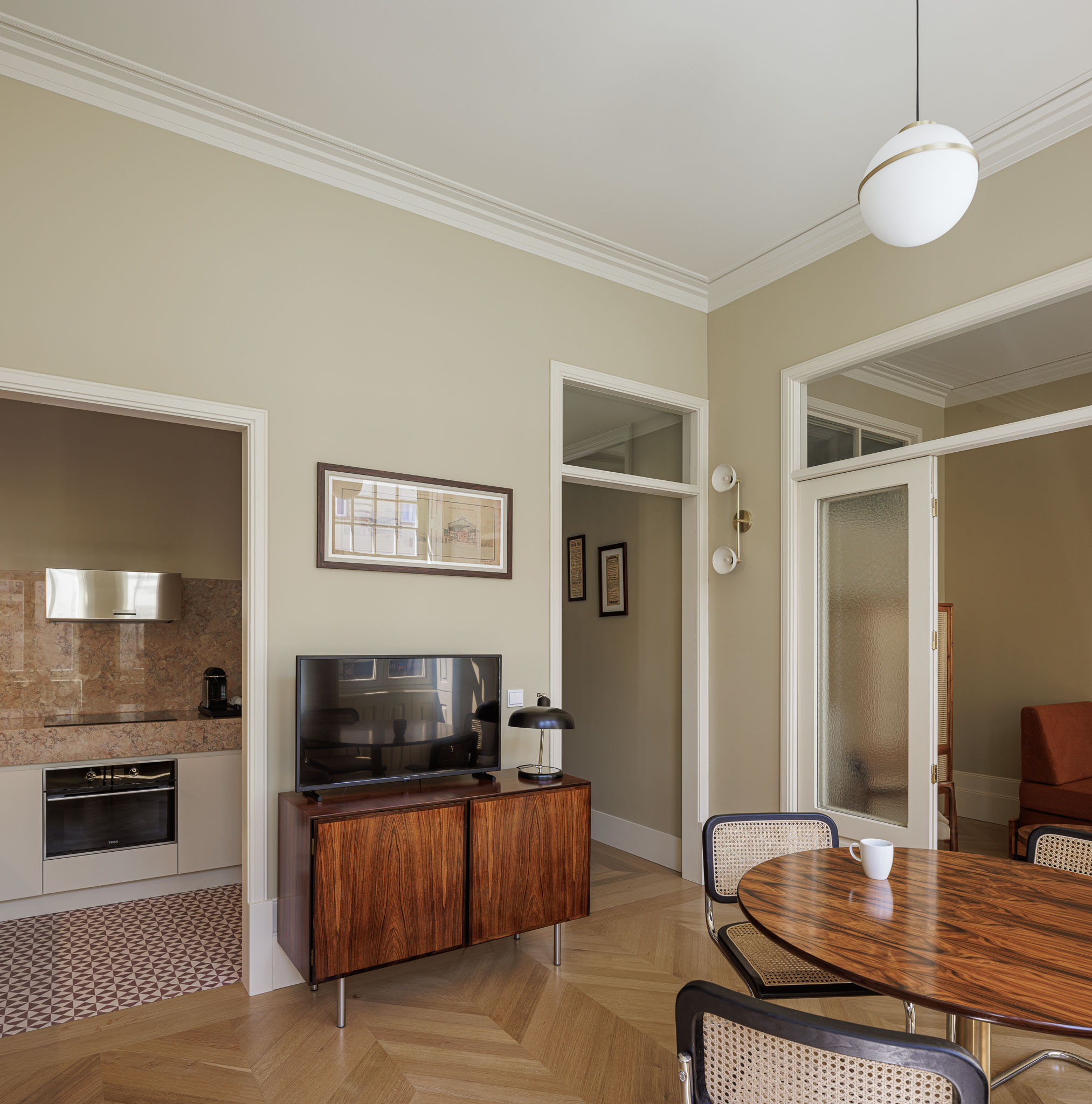 Sala de jantar: Mesa redonda em madeira escura com cadeiras de vime, aparador em madeira e acesso à cozinha. — Villa Theatro arquitetura arquitectos aliados em Braga