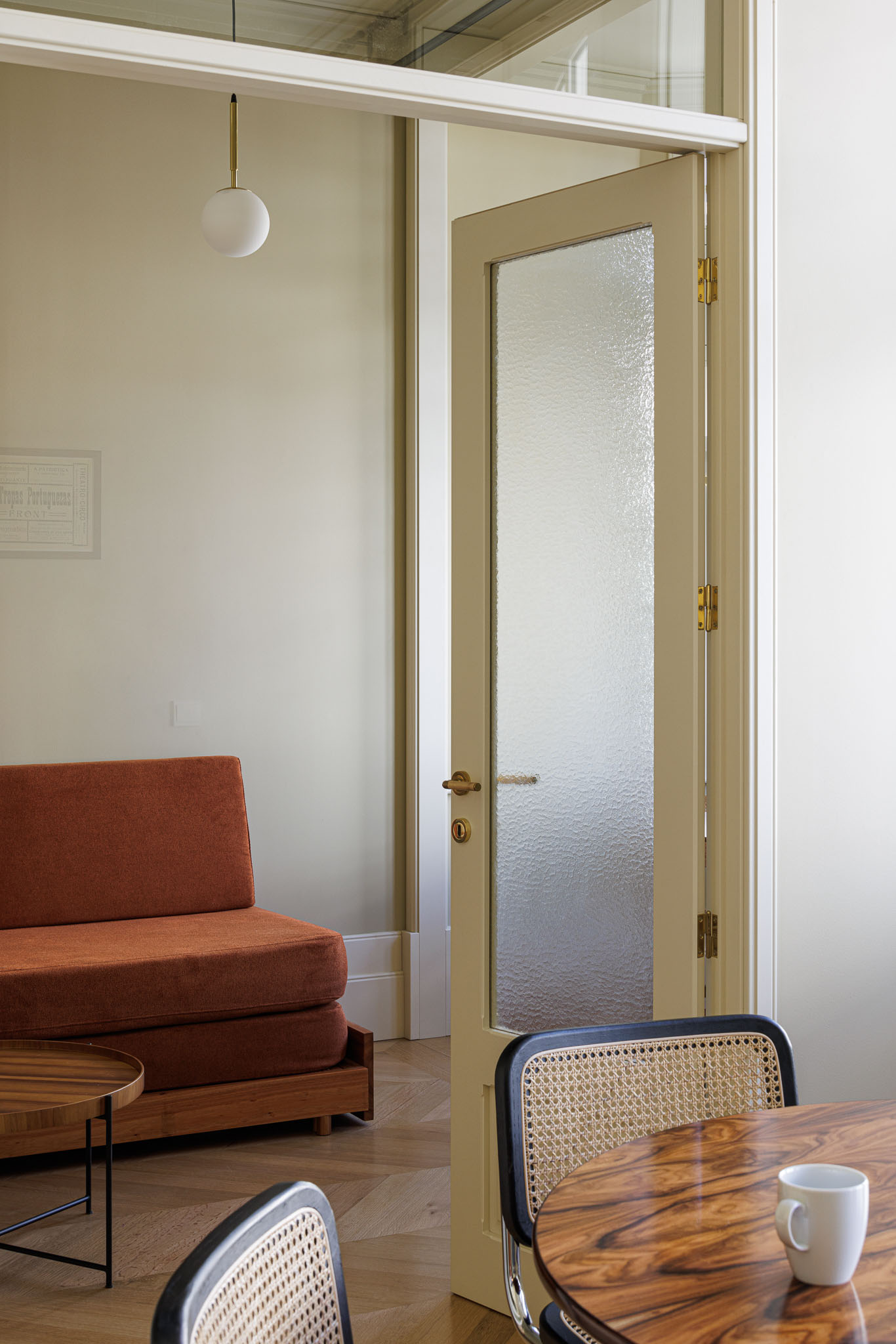 Sala de estar: Sofá laranja, mesa de apoio em madeira e porta de vidro texturizado, com pavimento em madeira clara. — Villa Theatro arquitetura arquitectos aliados em Braga