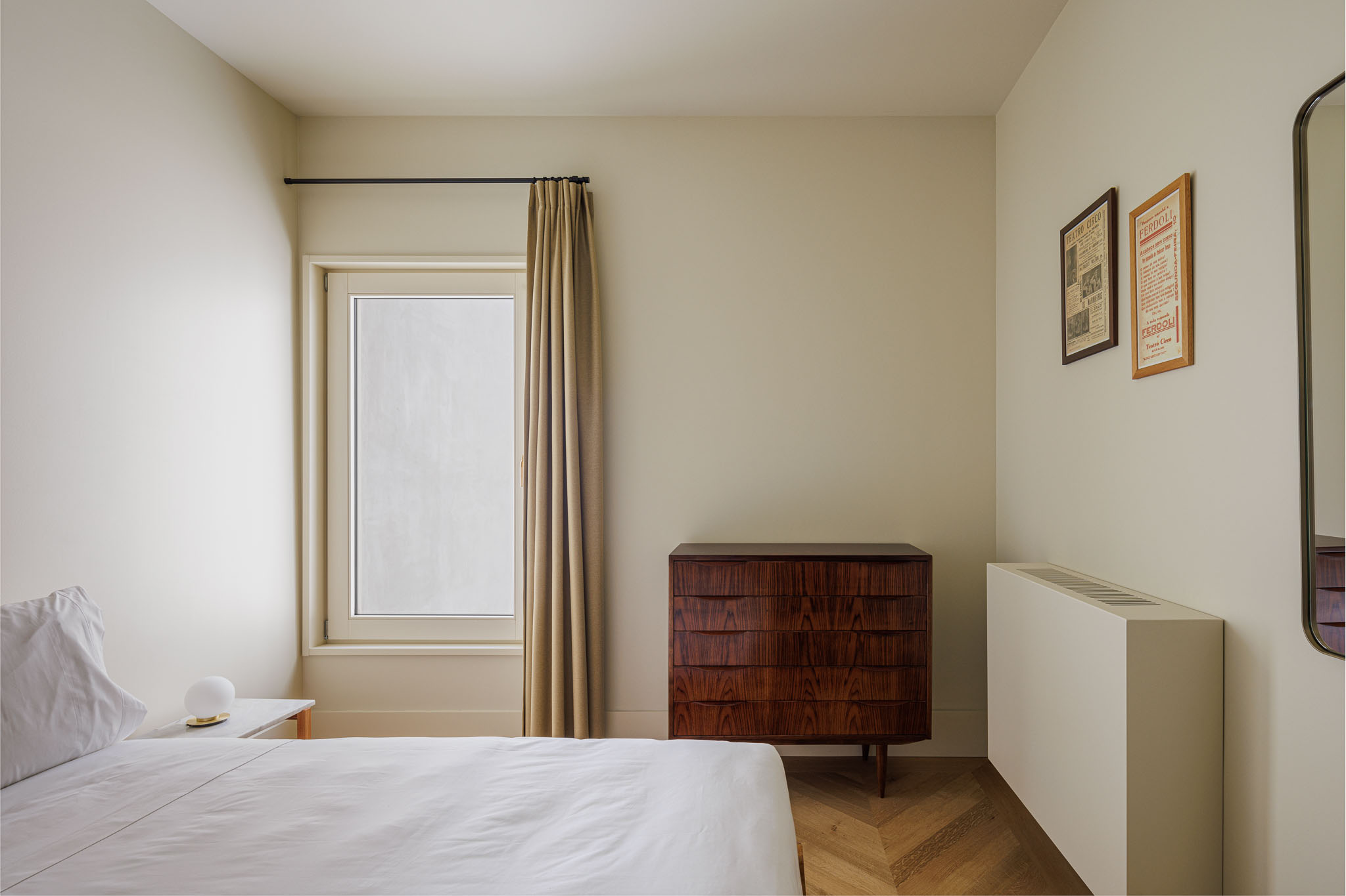 Quarto: Cama com roupa de cama branca, cómoda em madeira escura e cortina bege, com pavimento em madeira clara. — Villa Theatro arquitetura arquitectos aliados em Braga