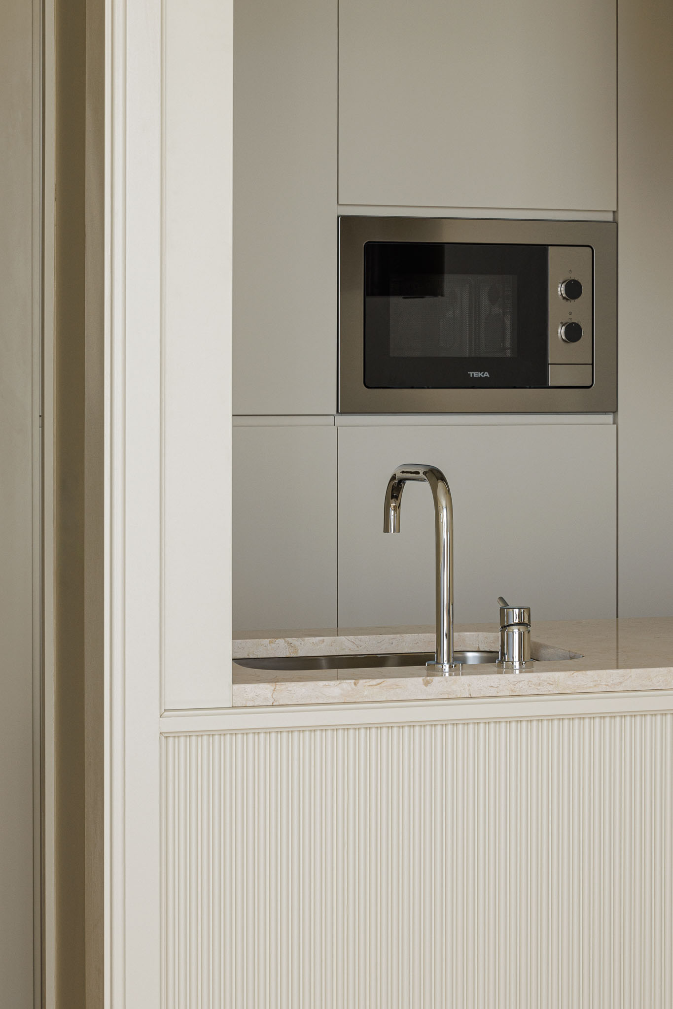 Cozinha: Detalhe do microondas e lavatório em inox, com bancada em mármore rosa e armários brancos. — Villa Theatro arquitetura arquitectos aliados em Braga