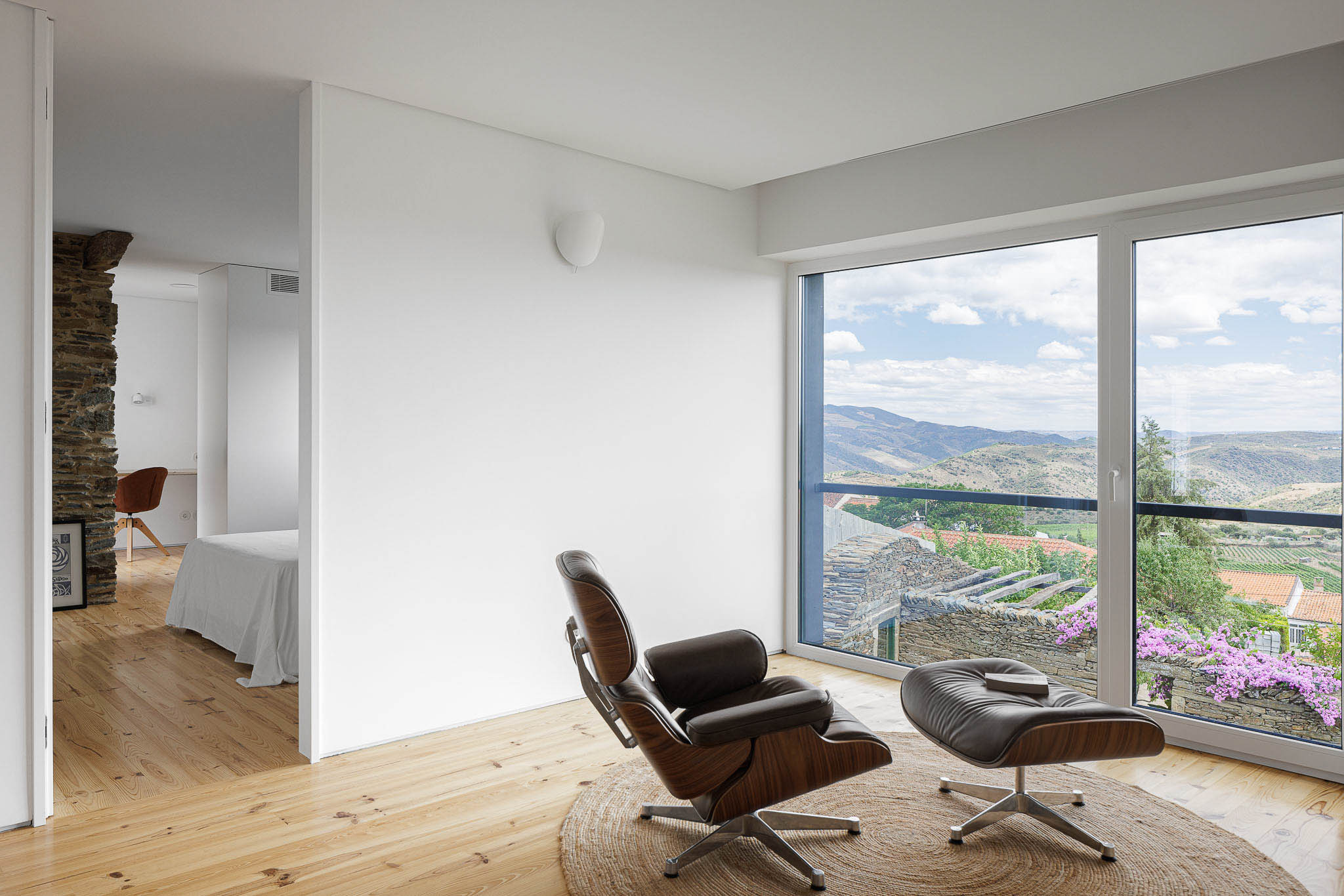 Sala de estar: Poltrona de couro e vista panorâmica para a paisagem. Pavimento em madeira e tapete de juta. — Casa Caldeira arquitetura Filipe Pina Arquitectura em Vila Nova de Foz Côa