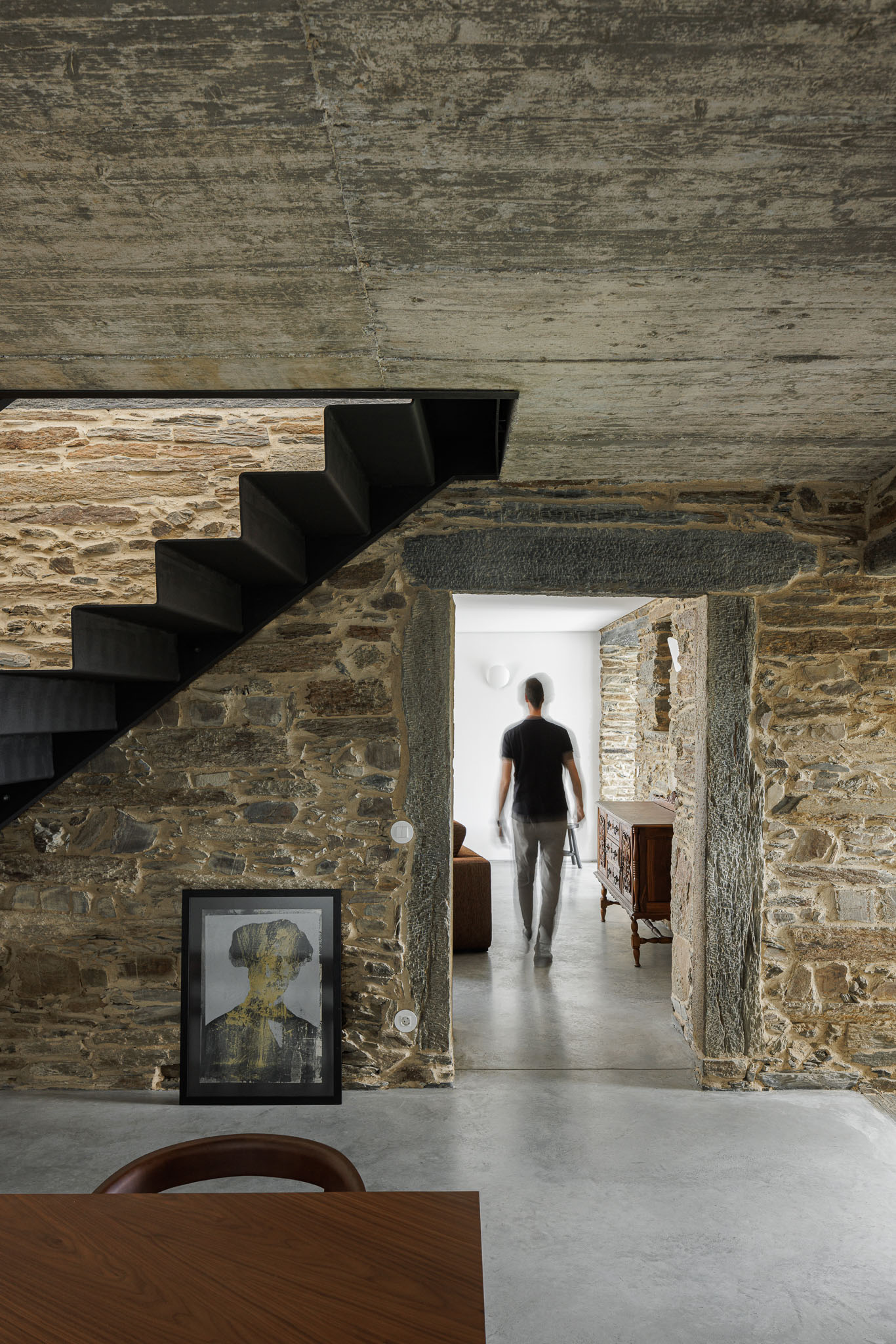 Sala de jantar: Escadas pretas, parede em pedra e teto em betão. Pavimento em cimento afagado. — Casa Caldeira arquitetura Filipe Pina Arquitectura em Vila Nova de Foz Côa