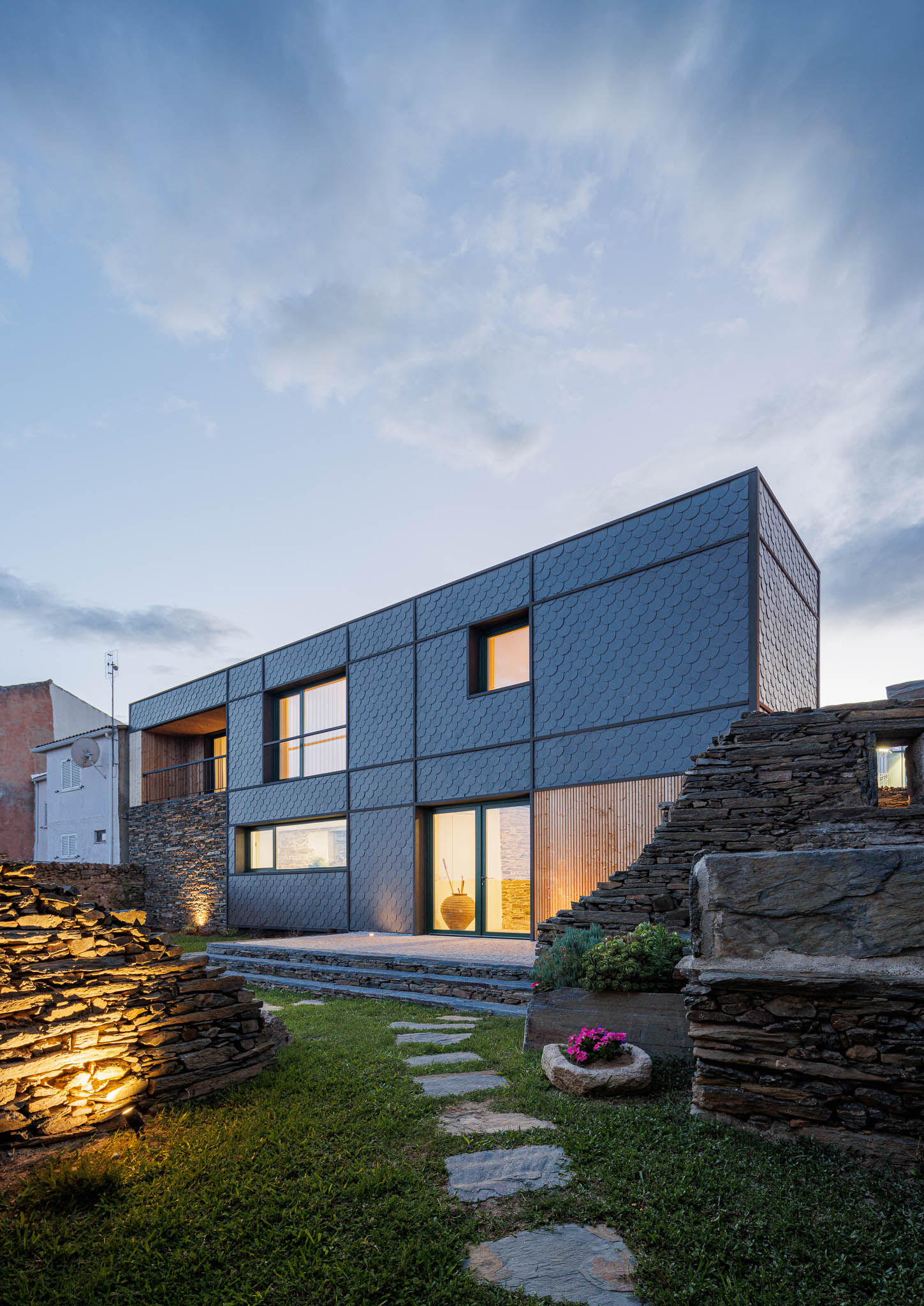 Exterior: Casa com revestimento em ardósia, integrada em ruínas de pedra e relvado. Iluminação exterior. — Casa Caldeira arquitetura Filipe Pina Arquitectura em Vila Nova de Foz Côa