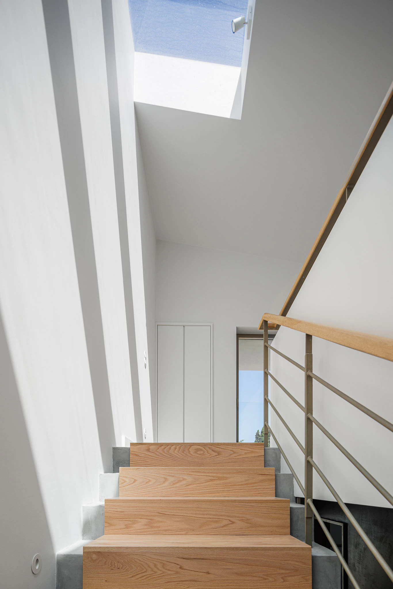 Escada de madeira com claraboia, parede branca e corrimão metálico. Design interior que valoriza a luz natural. — Casas do Pinhal arquitetura Pk Arquitetos em Estoril