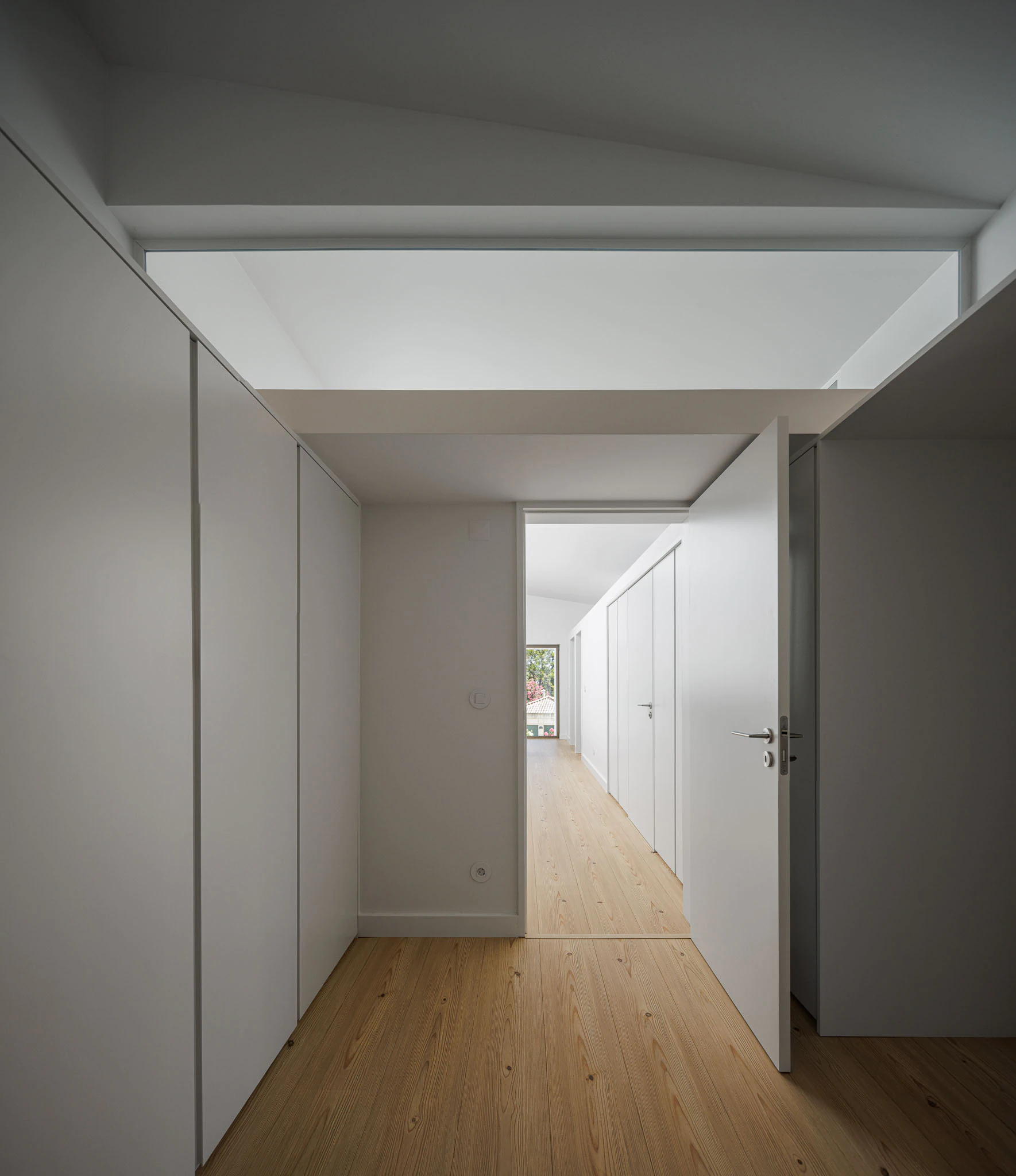 Corredor com armários brancos, claraboia e chão de madeira clara. Design minimalista e luminoso. — Casas do Pinhal arquitetura Pk Arquitetos em Estoril