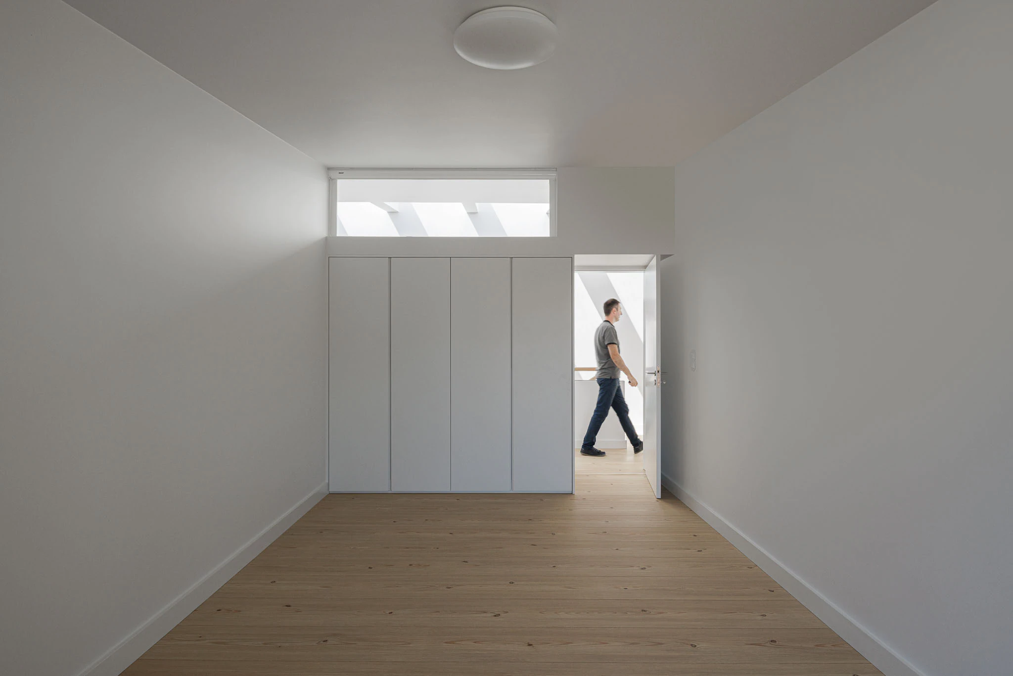 Quarto com armários brancos, claraboia e chão de madeira clara. Design minimalista e luminoso. — Casas do Pinhal arquitetura Pk Arquitetos em Estoril