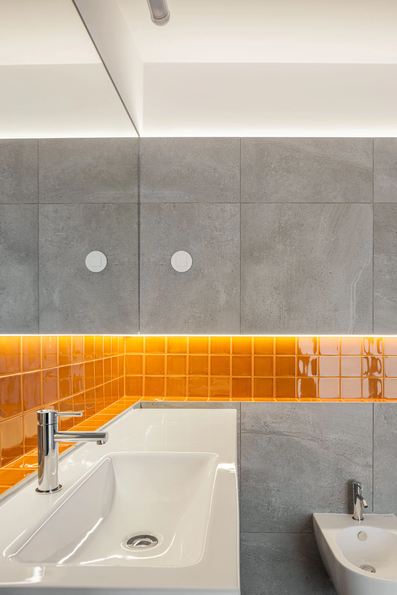 Casa de banho com azulejos cinzentos e faixa laranja, lavatório branco e bidé. Estilo minimalista e moderno. — Casas do Pinhal arquitetura Pk Arquitetos em Estoril