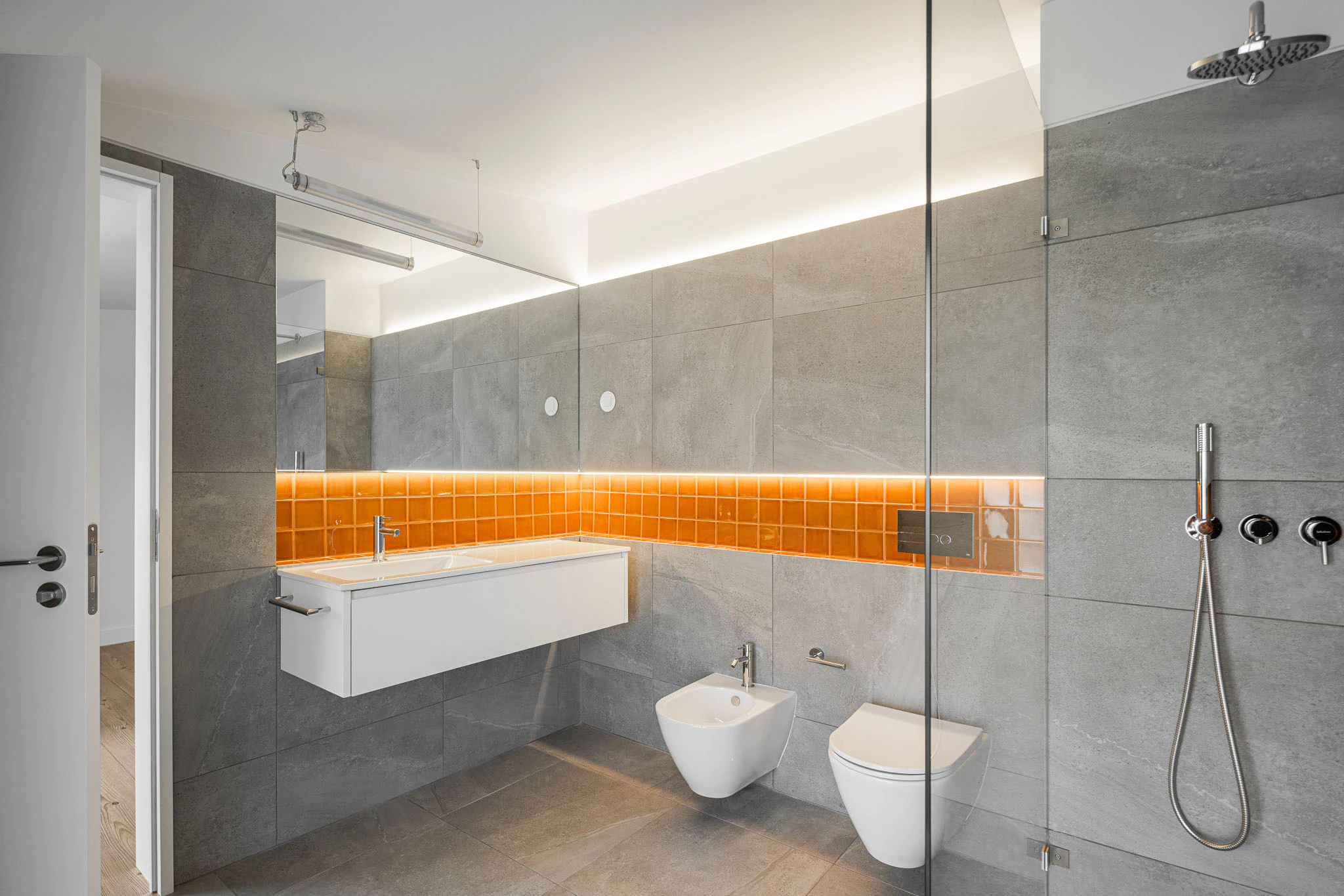 Casa de banho com azulejos cinzentos e laranja, lavatório branco e duche. Estilo moderno e funcional. — Casas do Pinhal arquitetura Pk Arquitetos em Estoril