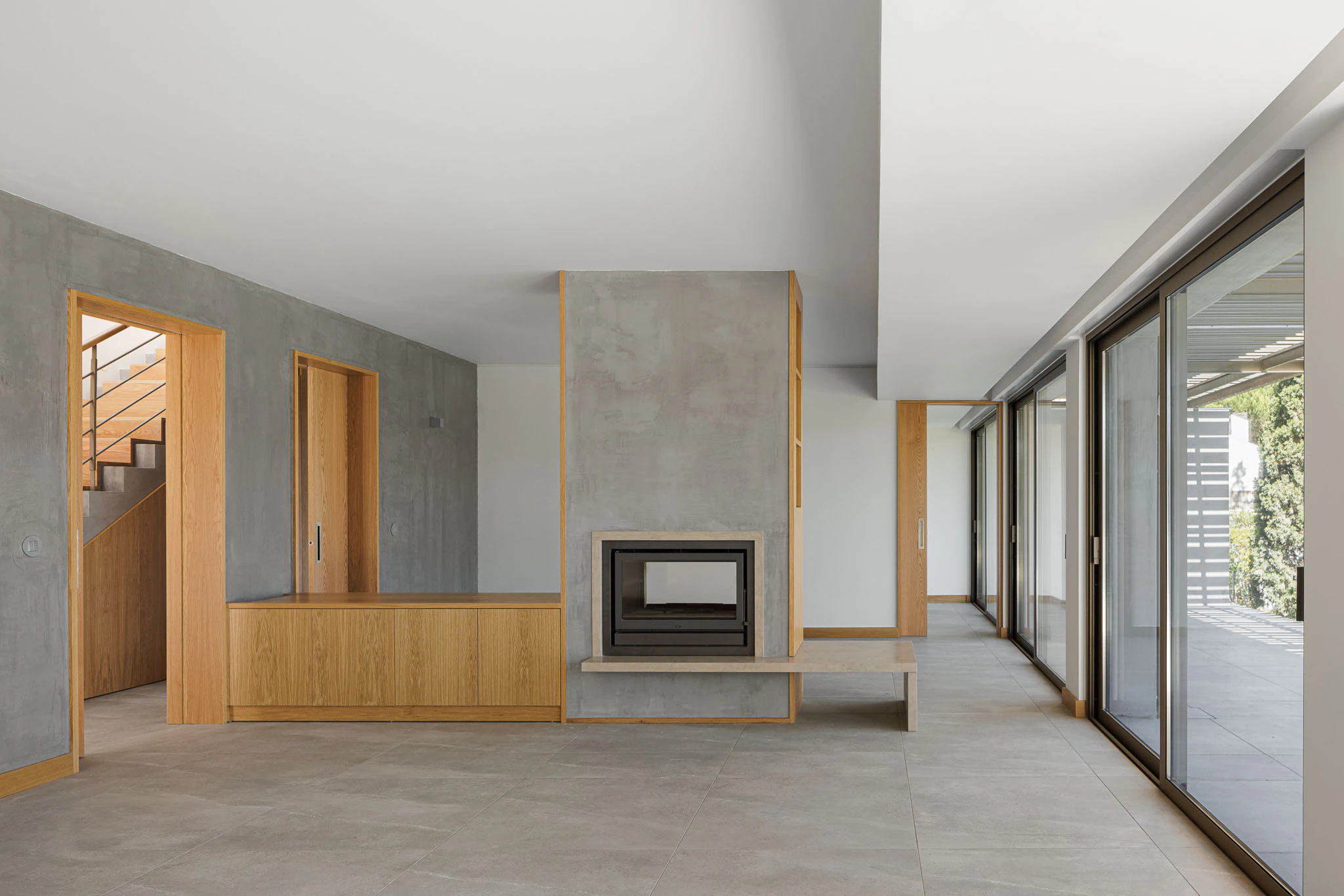 Sala de estar com lareira, estantes de madeira e grandes janelas. Design interior moderno e acolhedor. — Casas do Pinhal arquitetura Pk Arquitetos em Estoril