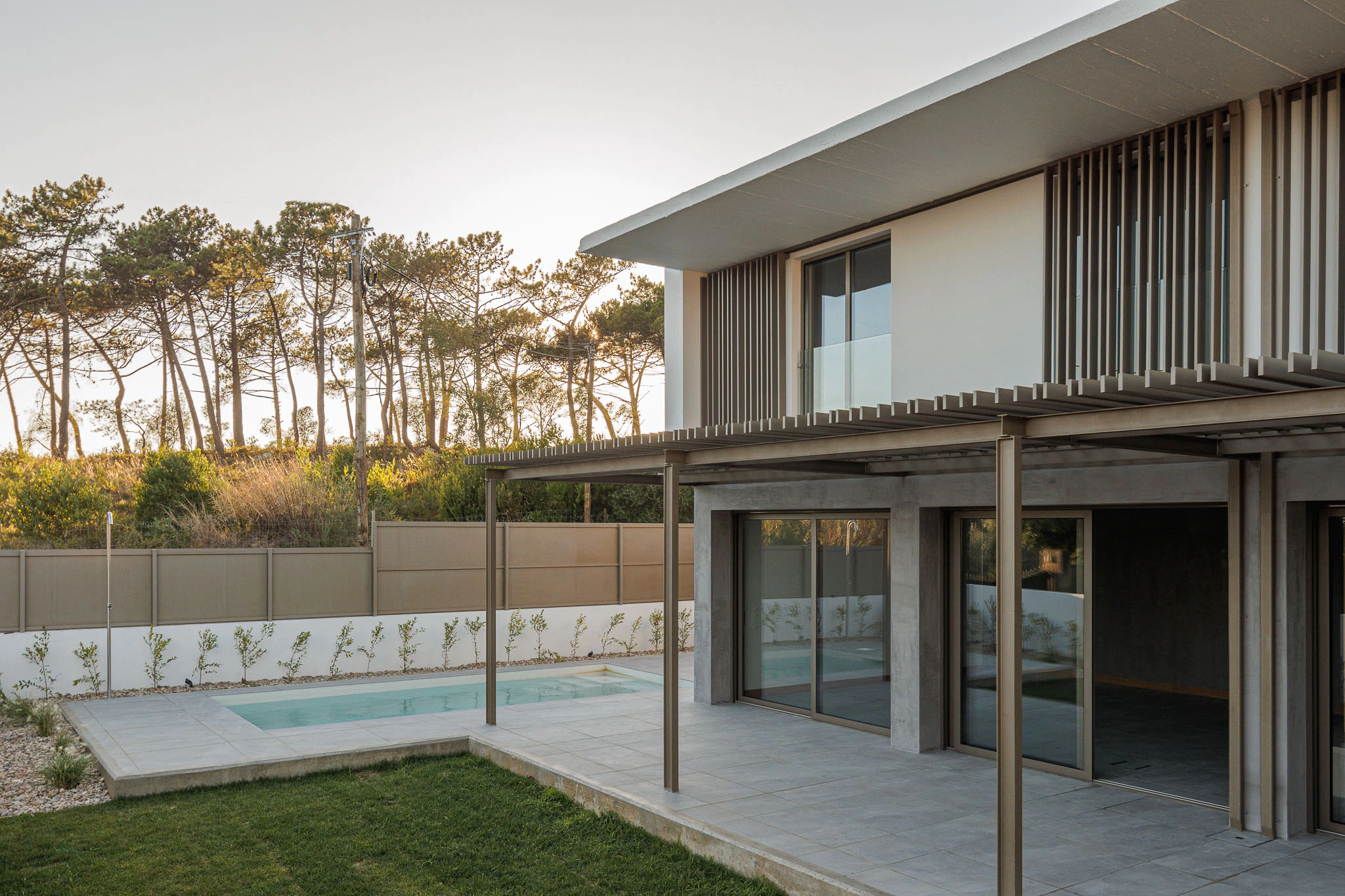 Exterior da casa com piscina, pérgola metálica e vegetação. Arquitetura moderna e integrada no exterior. — Casas do Pinhal arquitetura Pk Arquitetos em Estoril