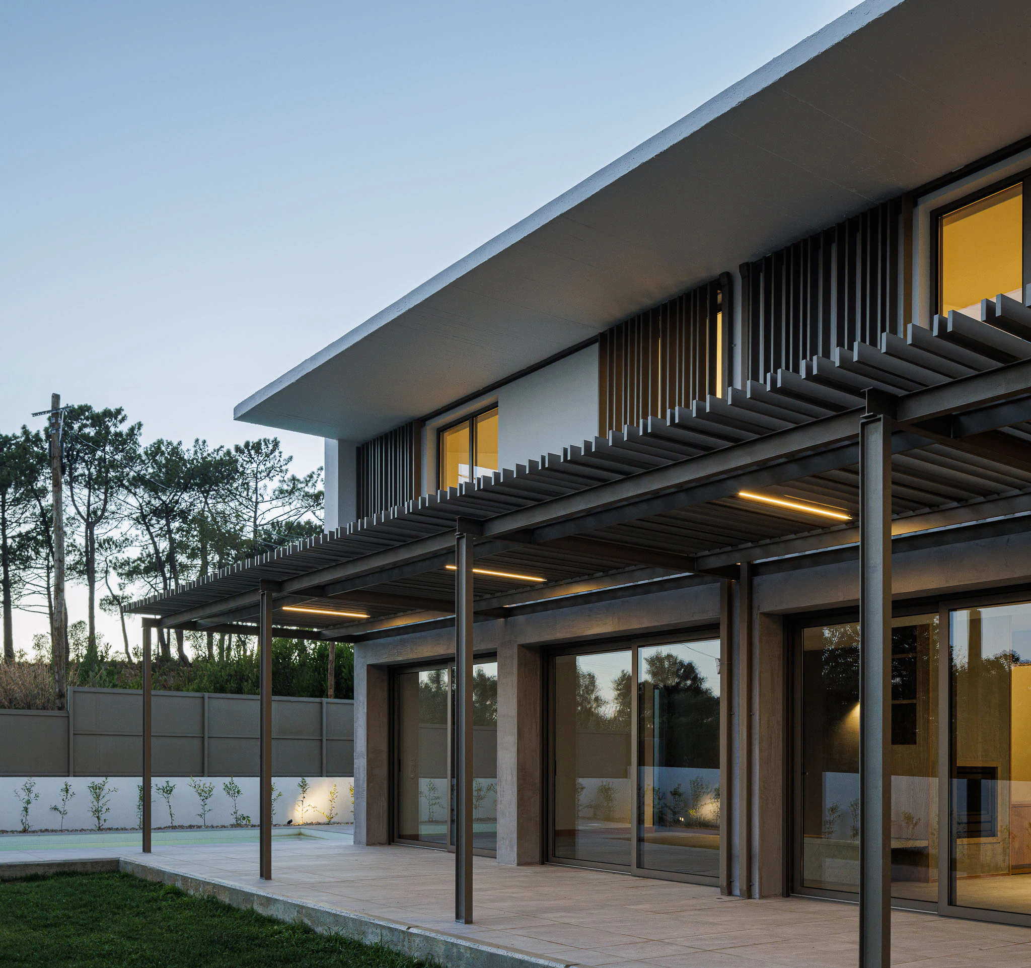 Fachada posterior da casa com pérgola metálica e iluminação. Arquitetura moderna e elegante. — Casas do Pinhal arquitetura Pk Arquitetos em Estoril