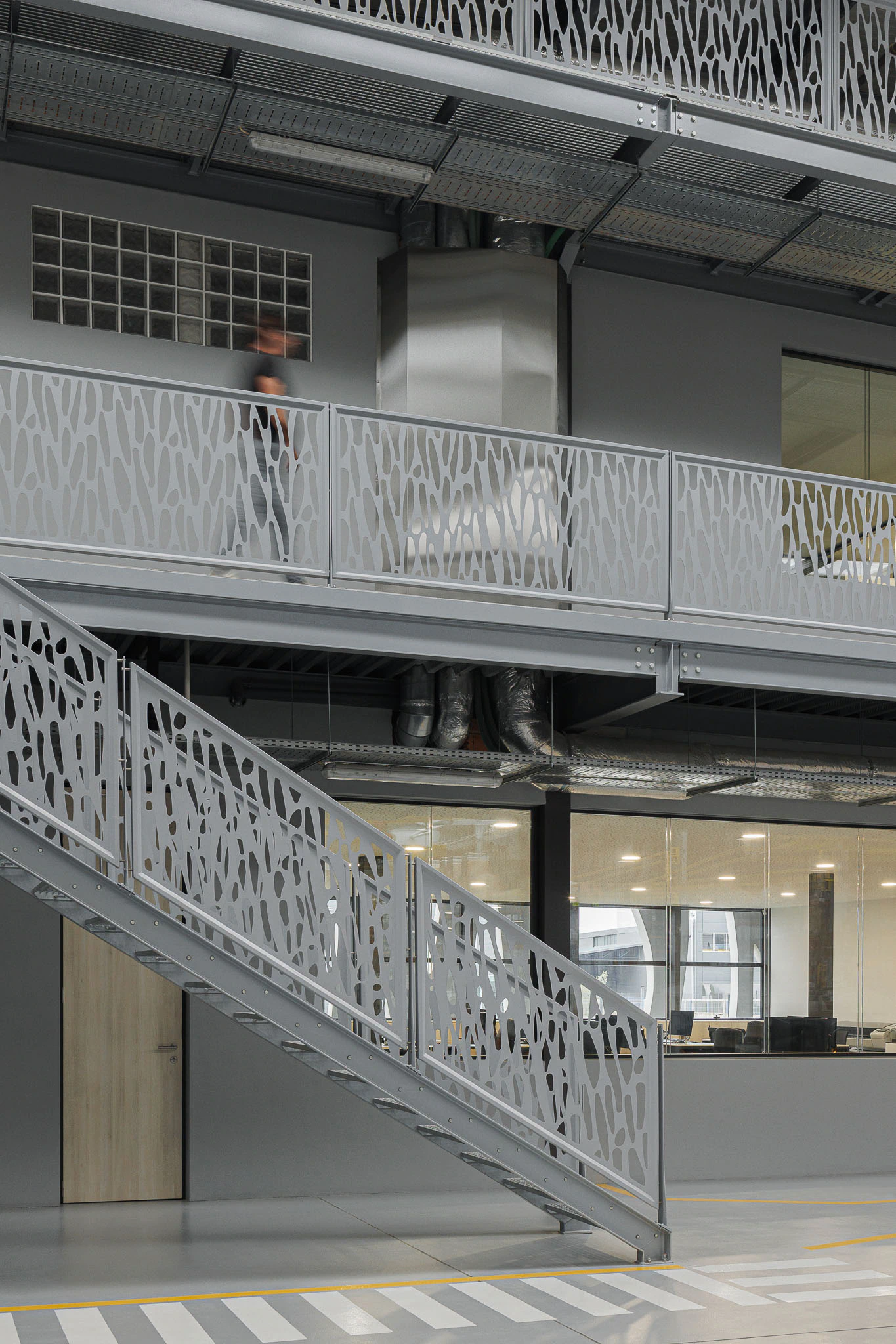 Interior: Escada metálica com padrão orgânico, ligando pisos em espaço industrial com escritórios envidraçados. — Ferneto arquitetura Rómulo Neto Arquitectos em Vagos