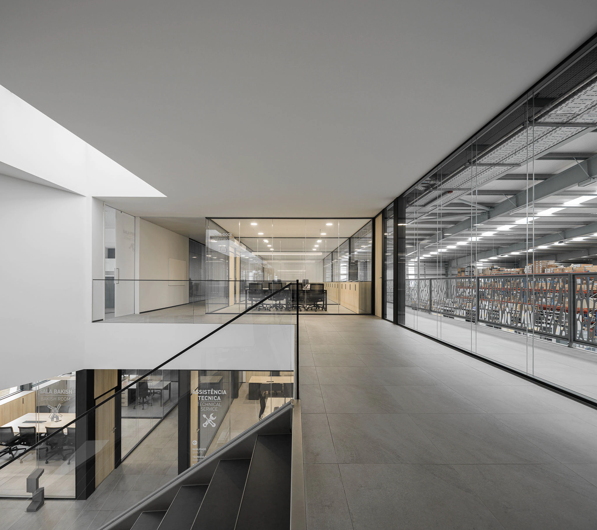 Interior: Corredor superior com vista para escritórios envidraçados e armazém industrial. — Ferneto arquitetura Rómulo Neto Arquitectos em Vagos