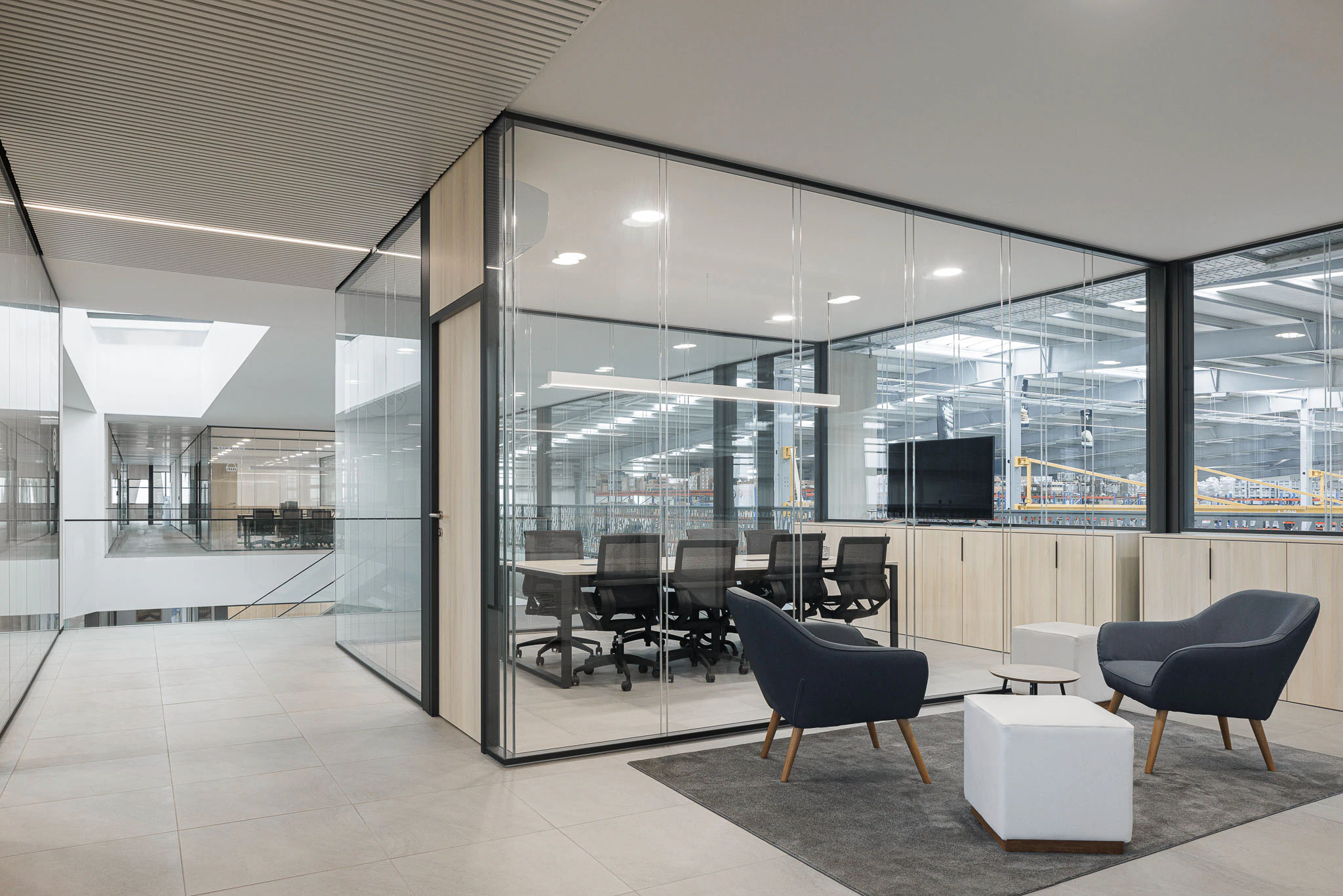 Interior: Sala de reuniões envidraçada com mobiliário moderno e vista para o armazém industrial. — Ferneto arquitetura Rómulo Neto Arquitectos em Vagos