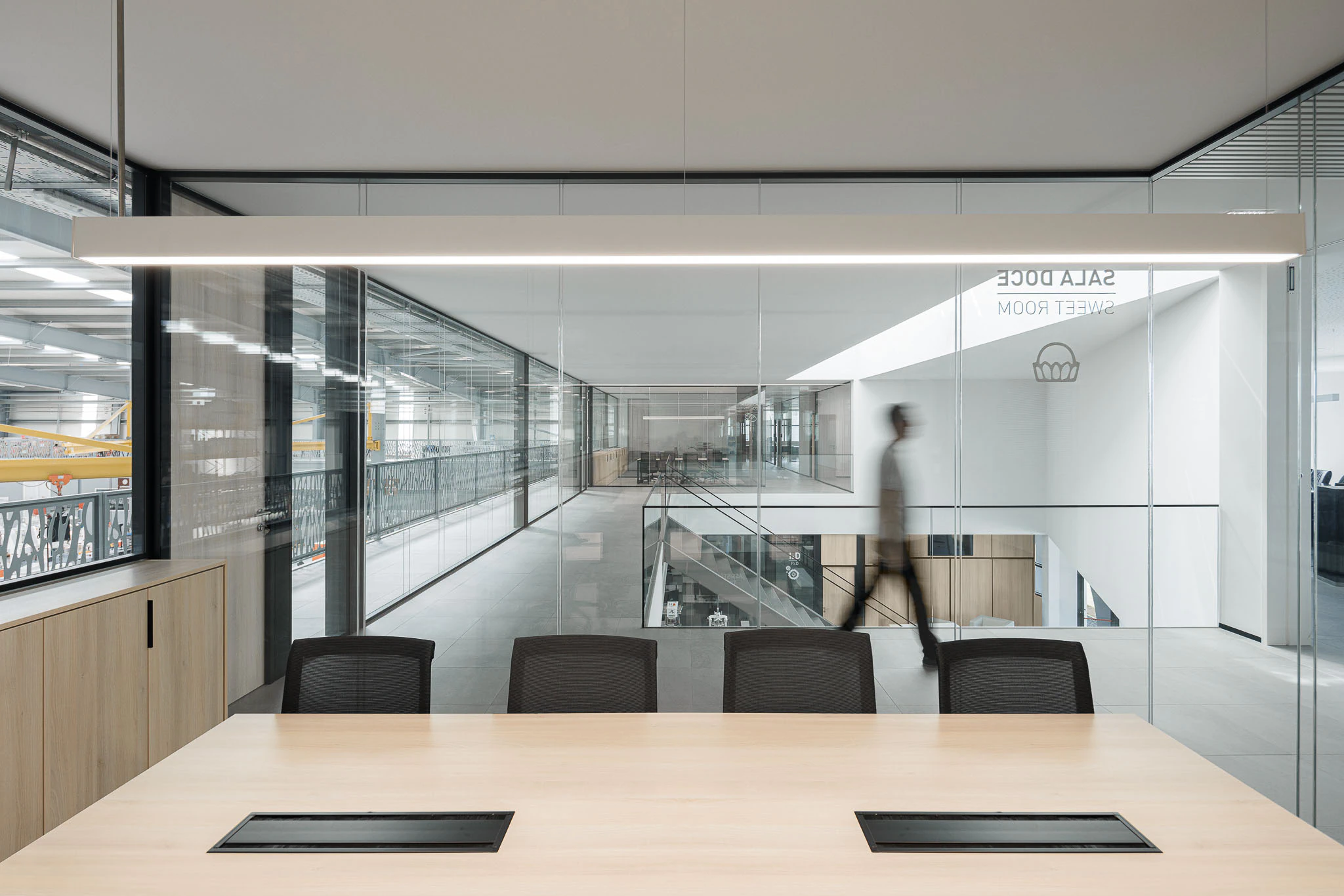 Interior: Sala de reuniões com mesa de madeira, cadeiras pretas e vista para o corredor e armazém. — Ferneto arquitetura Rómulo Neto Arquitectos em Vagos