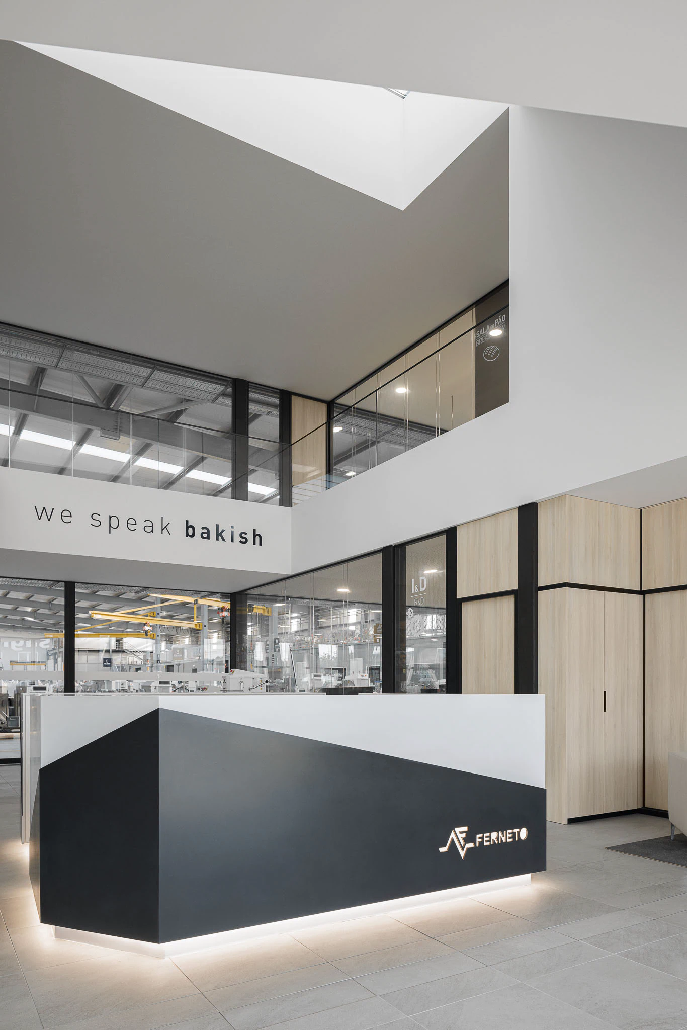 Interior: Detalhe do balcão de receção com logótipo iluminado e vista para o espaço industrial. — Ferneto arquitetura Rómulo Neto Arquitectos em Vagos