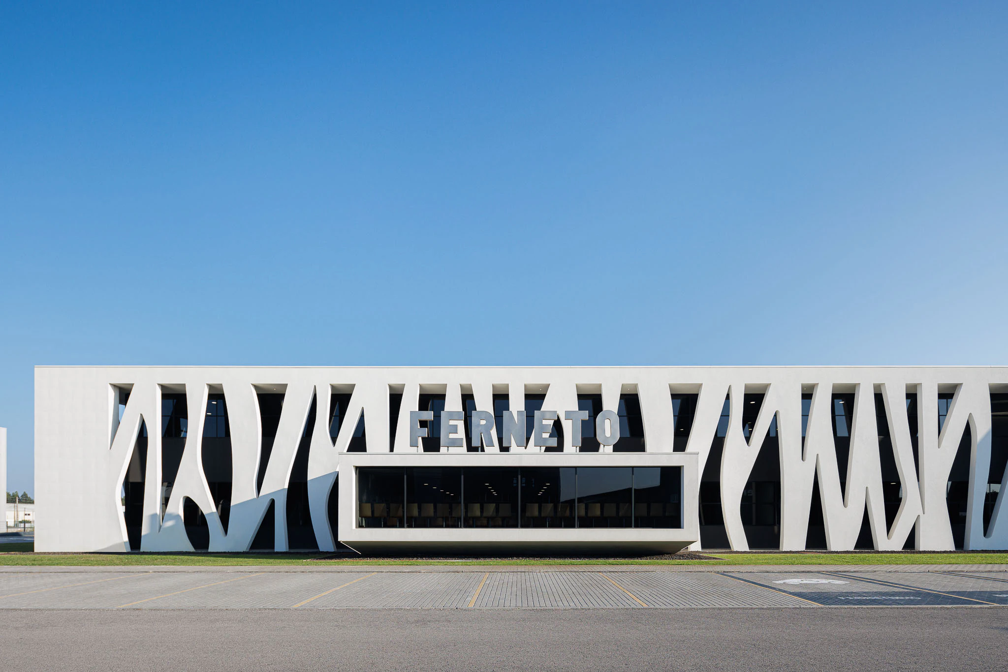 Exterior: Edifício industrial branco com fachada orgânica, estacionamento e céu azul. — Ferneto arquitetura Rómulo Neto Arquitectos em Vagos