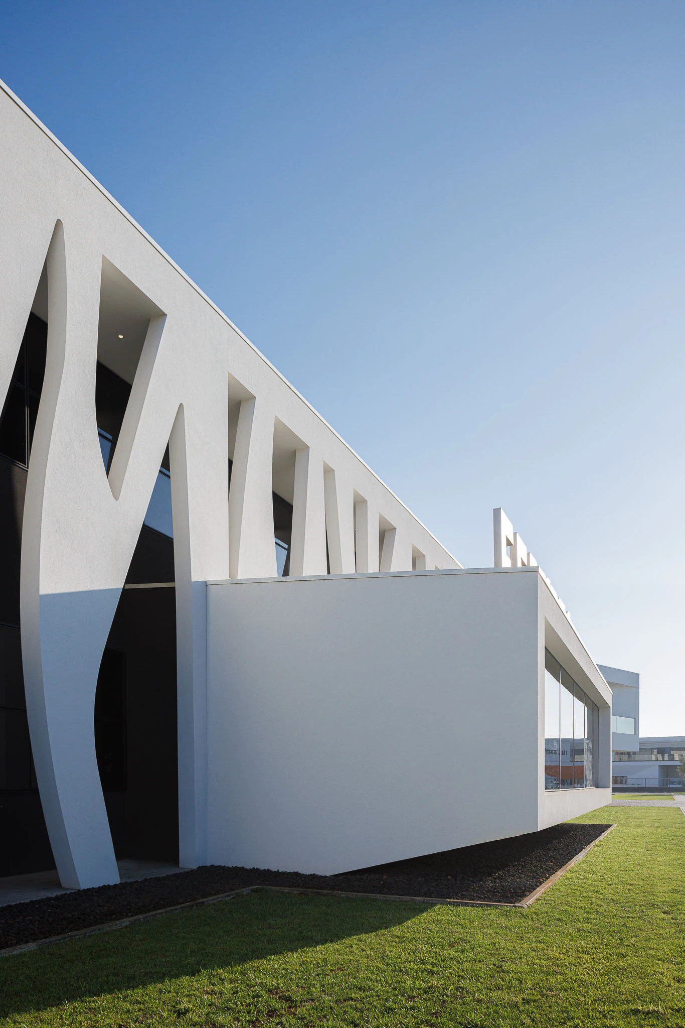 Exterior: Perspectiva lateral do edifício com fachada orgânica e zona ajardinada. — Ferneto arquitetura Rómulo Neto Arquitectos em Vagos