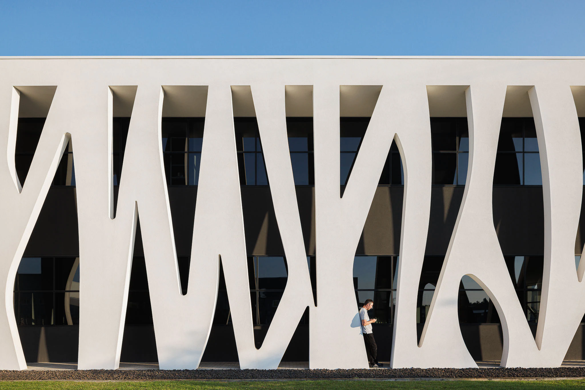 Exterior: Detalhe da fachada orgânica branca com janelas pretas e pessoa encostada. — Ferneto arquitetura Rómulo Neto Arquitectos em Vagos