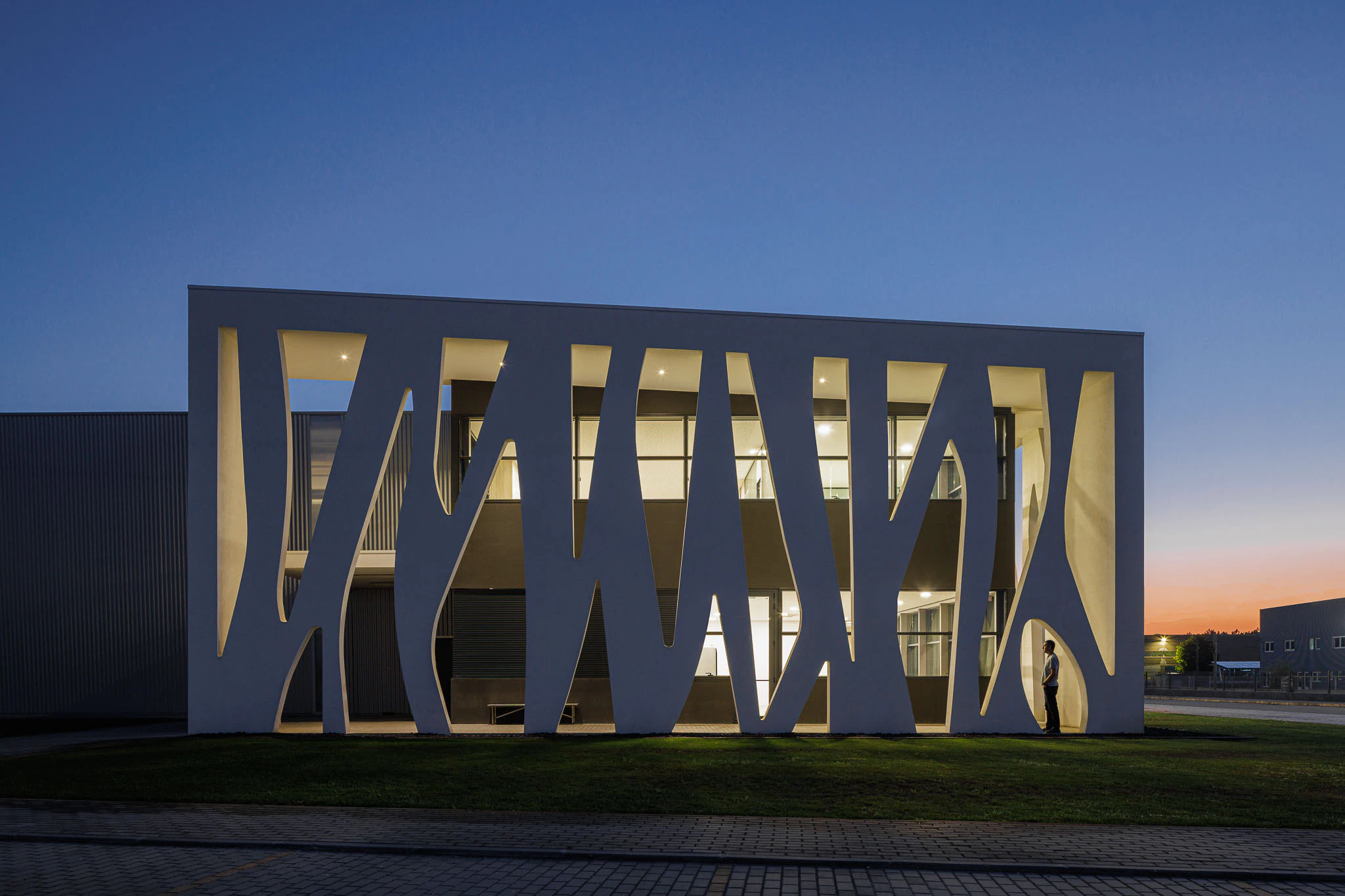 Exterior: Edifício com fachada orgânica iluminada, logótipo e sala de reuniões envidraçada. — Ferneto arquitetura Rómulo Neto Arquitectos em Vagos