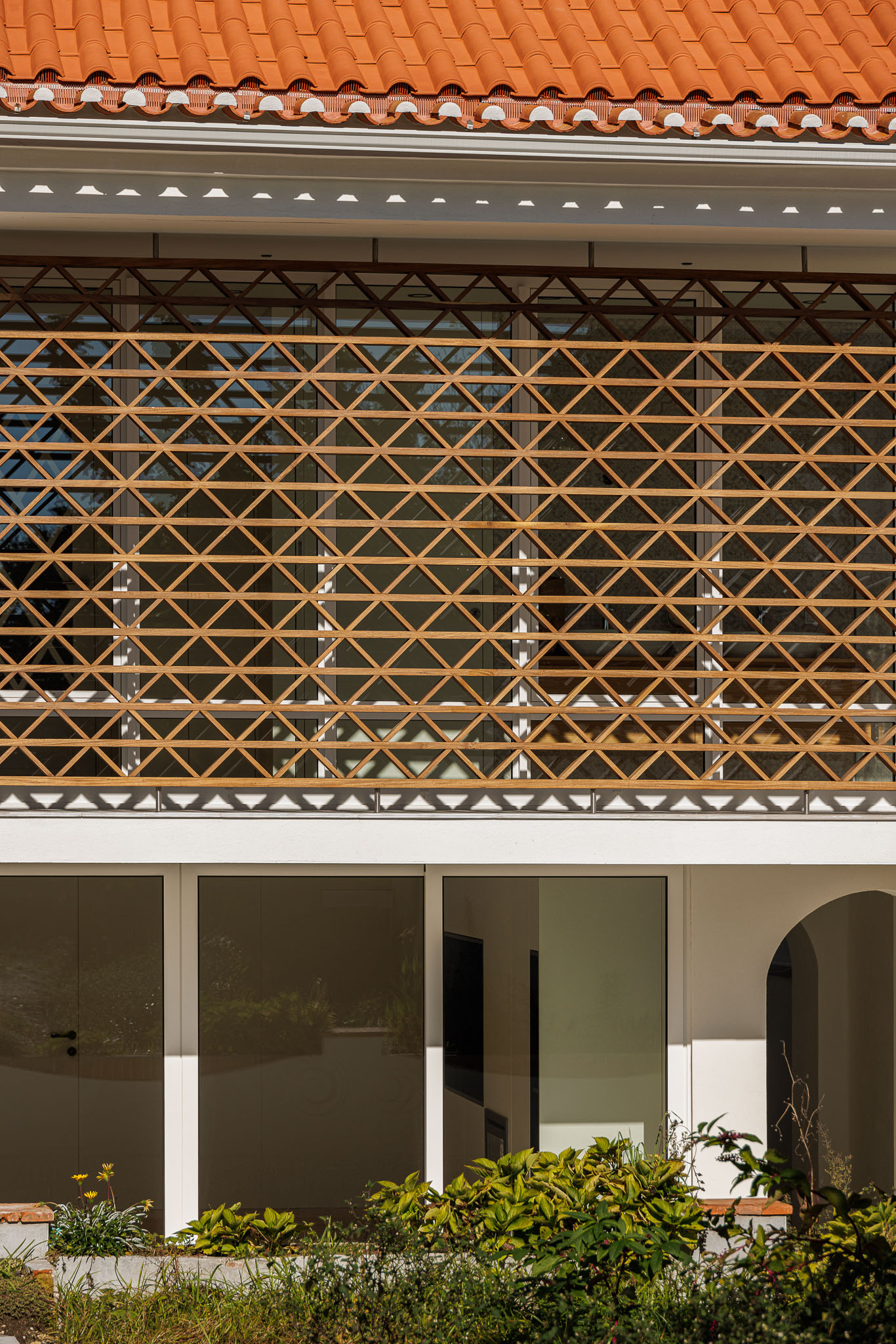 Fachada: Vista frontal da casa com grelha de madeira, janelas amplas e vegetação rasteira. — Casa dos anos 40 arquitetura Frari em Ílhavo
