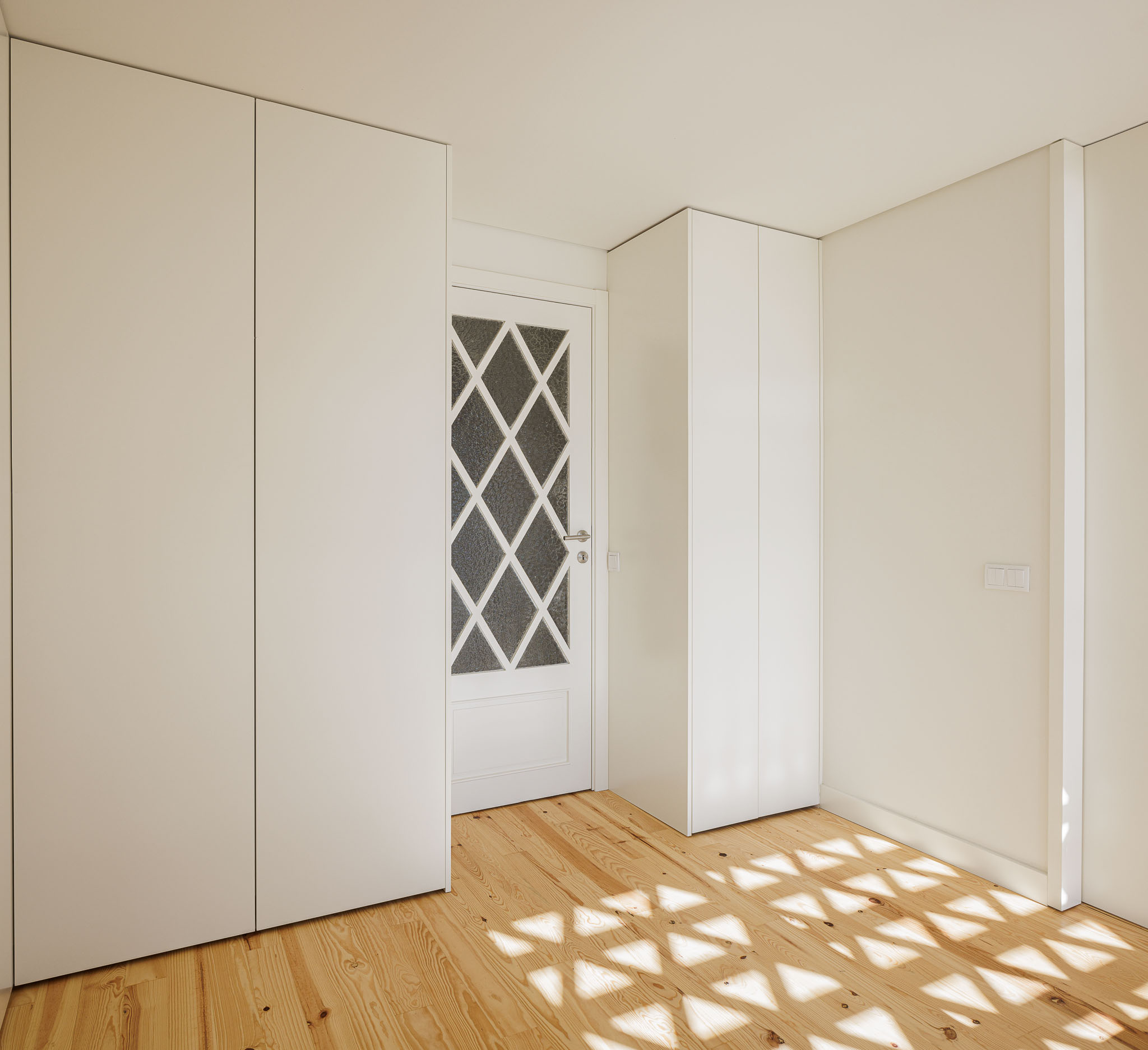 Quarto: Quarto com roupeiros embutidos brancos, porta com vidro trabalhado e pavimento em madeira clara. — Casa dos anos 40 arquitetura Frari em Ílhavo