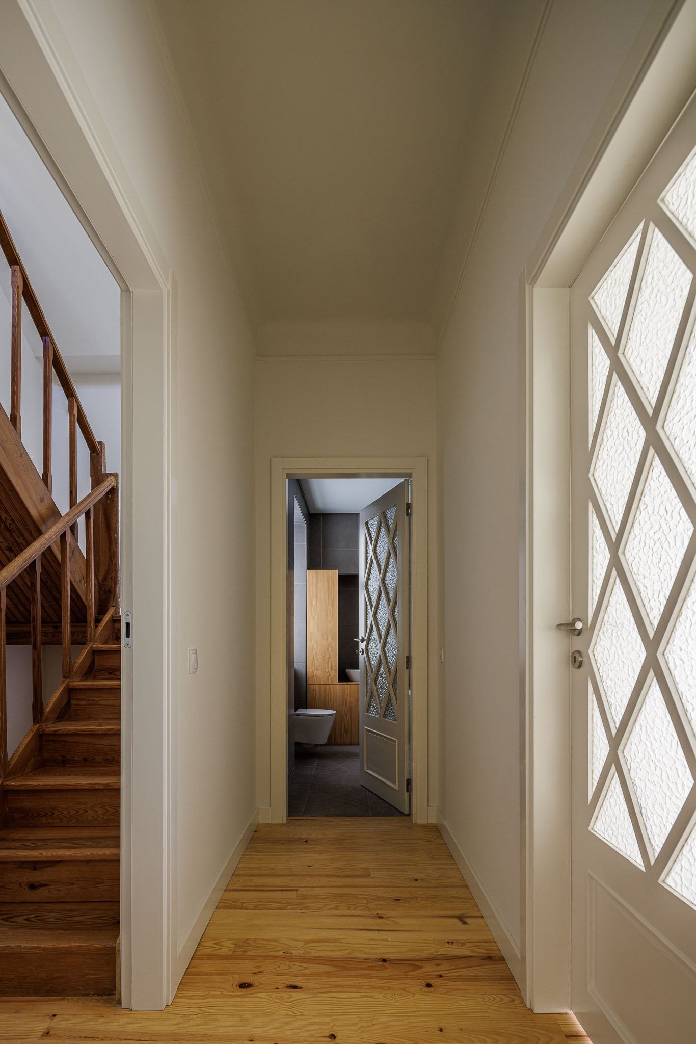 Corredor: Corredor com pavimento em madeira, porta com vidro trabalhado e acesso à escadaria em madeira. — Casa dos anos 40 arquitetura Frari em Ílhavo