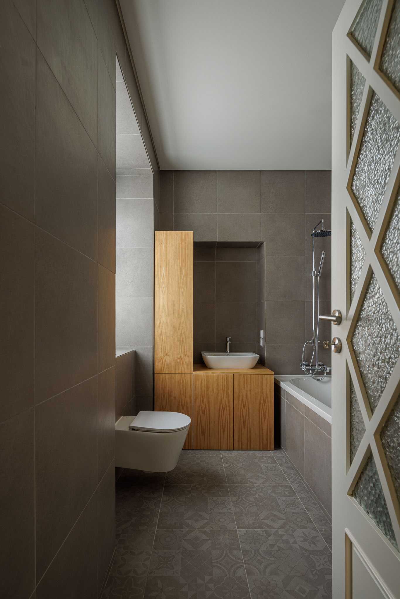 Casa de banho: Casa de banho com azulejos cinzentos, lavatório de pousar e porta com vidro trabalhado. — Casa dos anos 40 arquitetura Frari em Ílhavo
