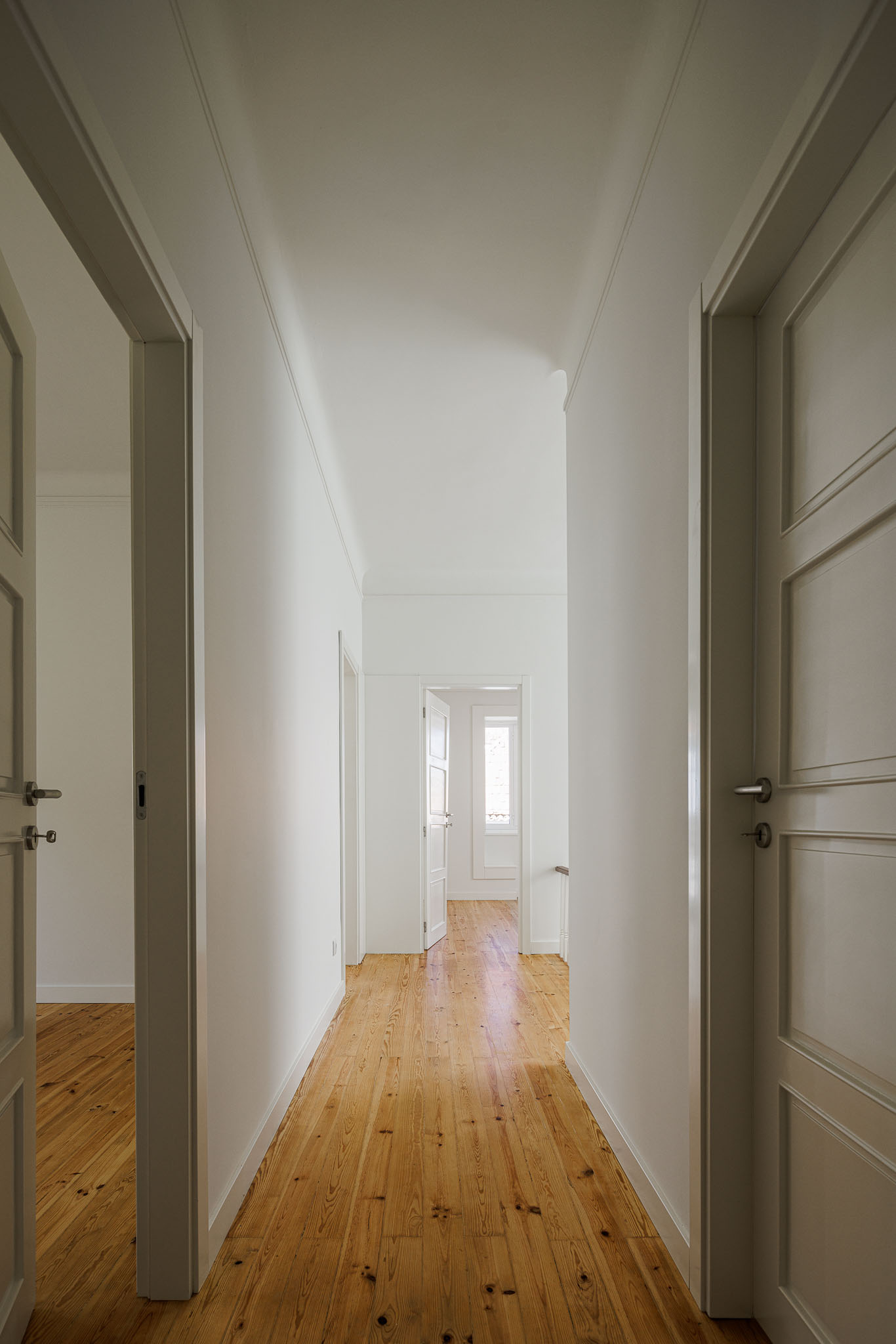 Corredor: Corredor com portas brancas e pavimento em madeira clara. — Casa dos anos 40 arquitetura Frari em Ílhavo