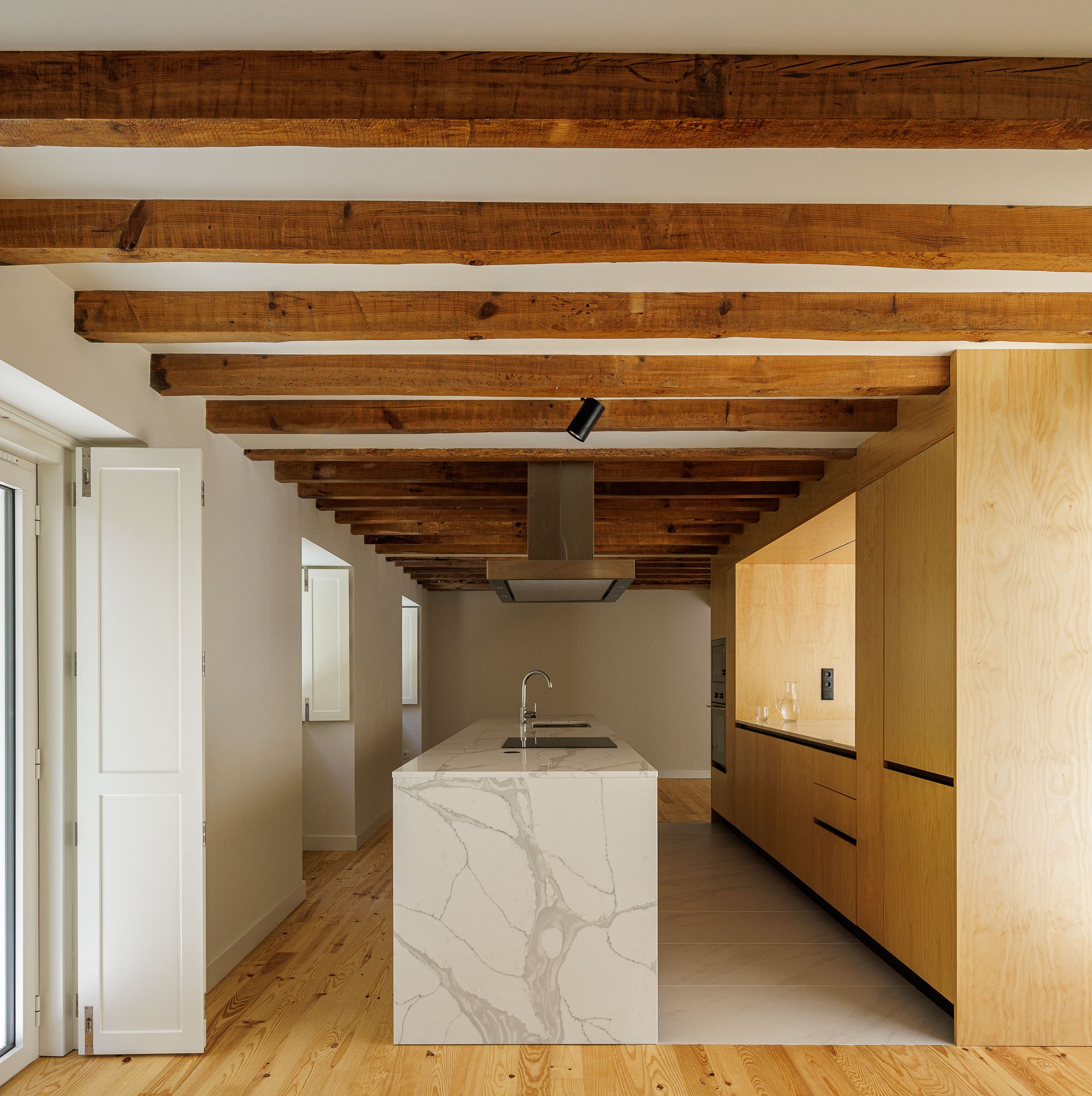 Cozinha: Cozinha com ilha em mármore, armários em madeira clara e teto com vigas de madeira aparente. — Casa dos anos 40 arquitetura Frari em Ílhavo