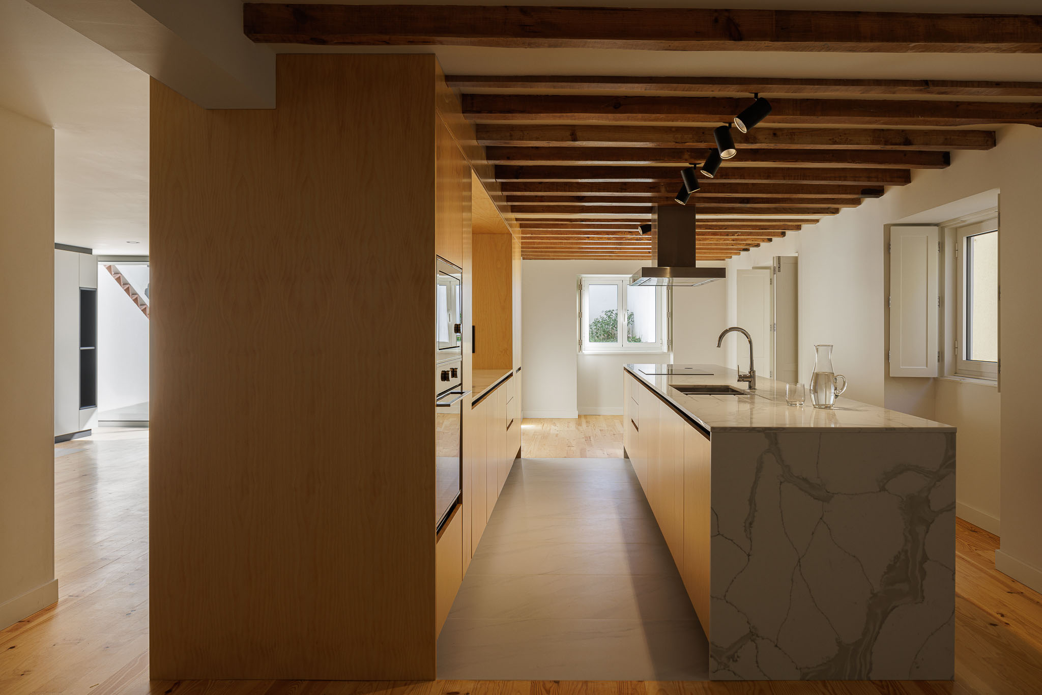 Cozinha: Cozinha com ilha em mármore, armários em madeira clara e teto com vigas de madeira aparente. — Casa dos anos 40 arquitetura Frari em Ílhavo
