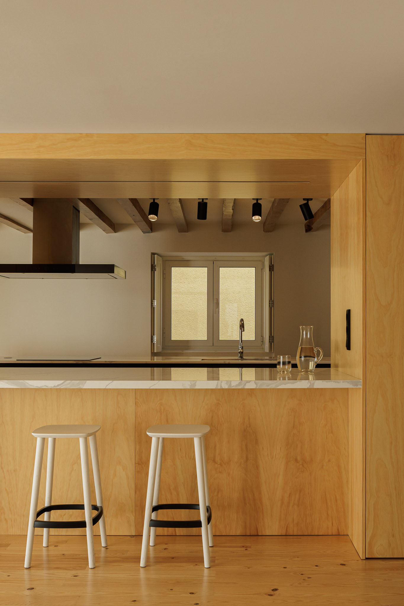 Cozinha: Detalhe da ilha da cozinha com bancos altos, armários em madeira clara e teto com vigas de madeira aparente. — Casa dos anos 40 arquitetura Frari em Ílhavo