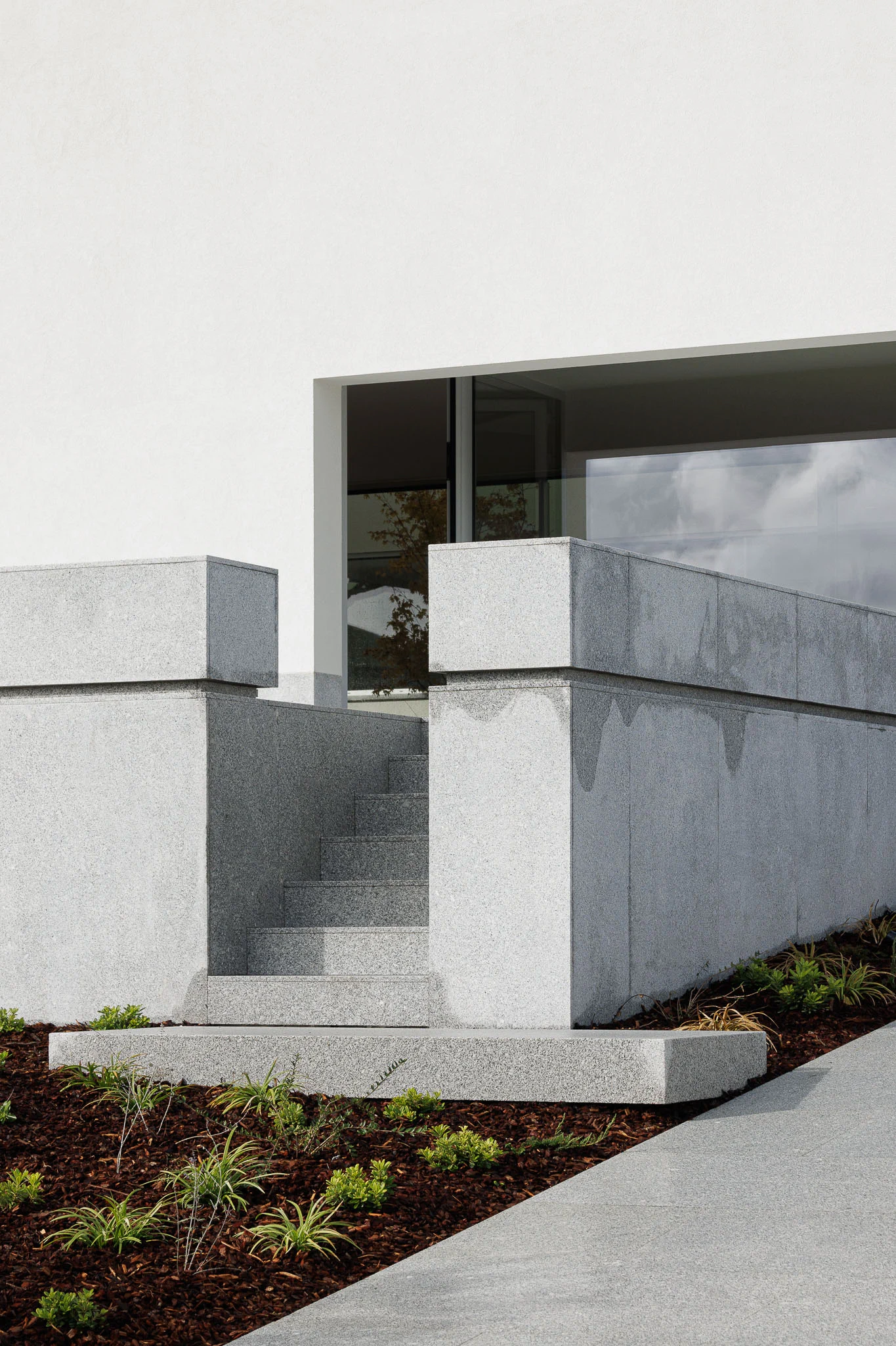 Detalhe da escadaria exterior em granito cinzento, com blocos geométricos e vegetação rasteira. — Casa em Santa Marinha arquitetura Helder da Rocha Arquitectos em Lousada