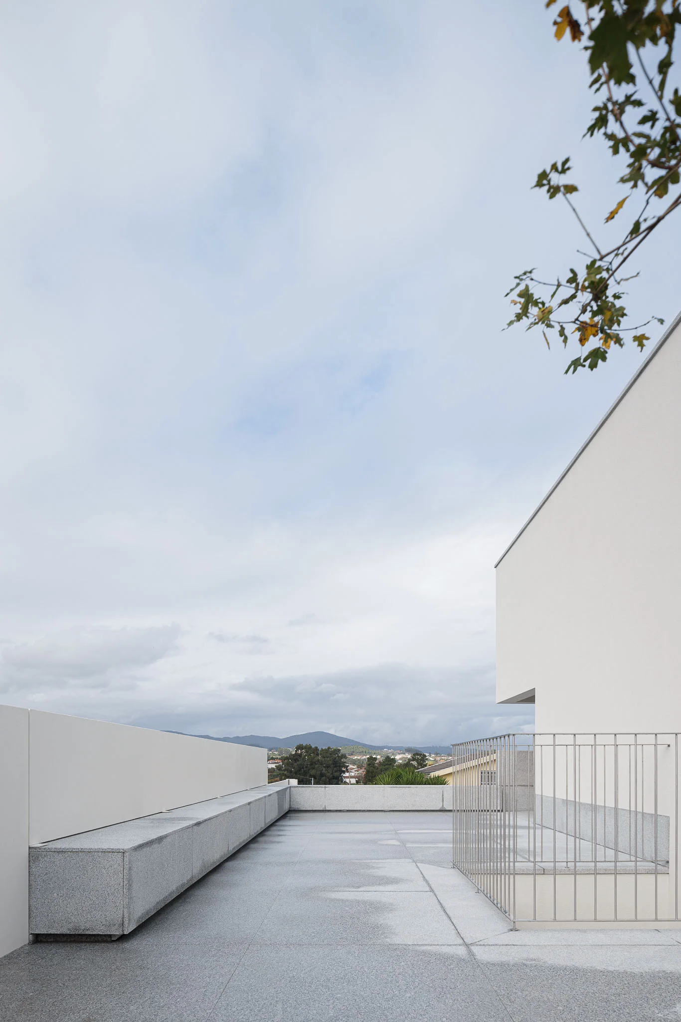 Terraço com pavimento em granito, banco embutido e vista para a paisagem. — Casa em Santa Marinha arquitetura Helder da Rocha Arquitectos em Lousada