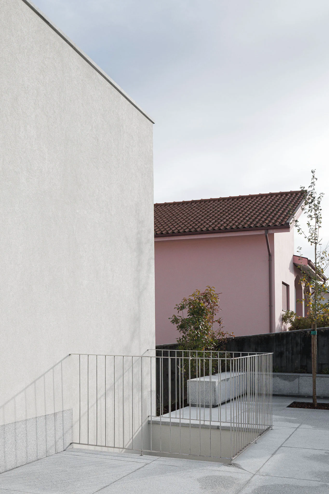 Detalhe do terraço com grade metálica, banco em granito e casa rosa vizinha ao fundo. — Casa em Santa Marinha arquitetura Helder da Rocha Arquitectos em Lousada