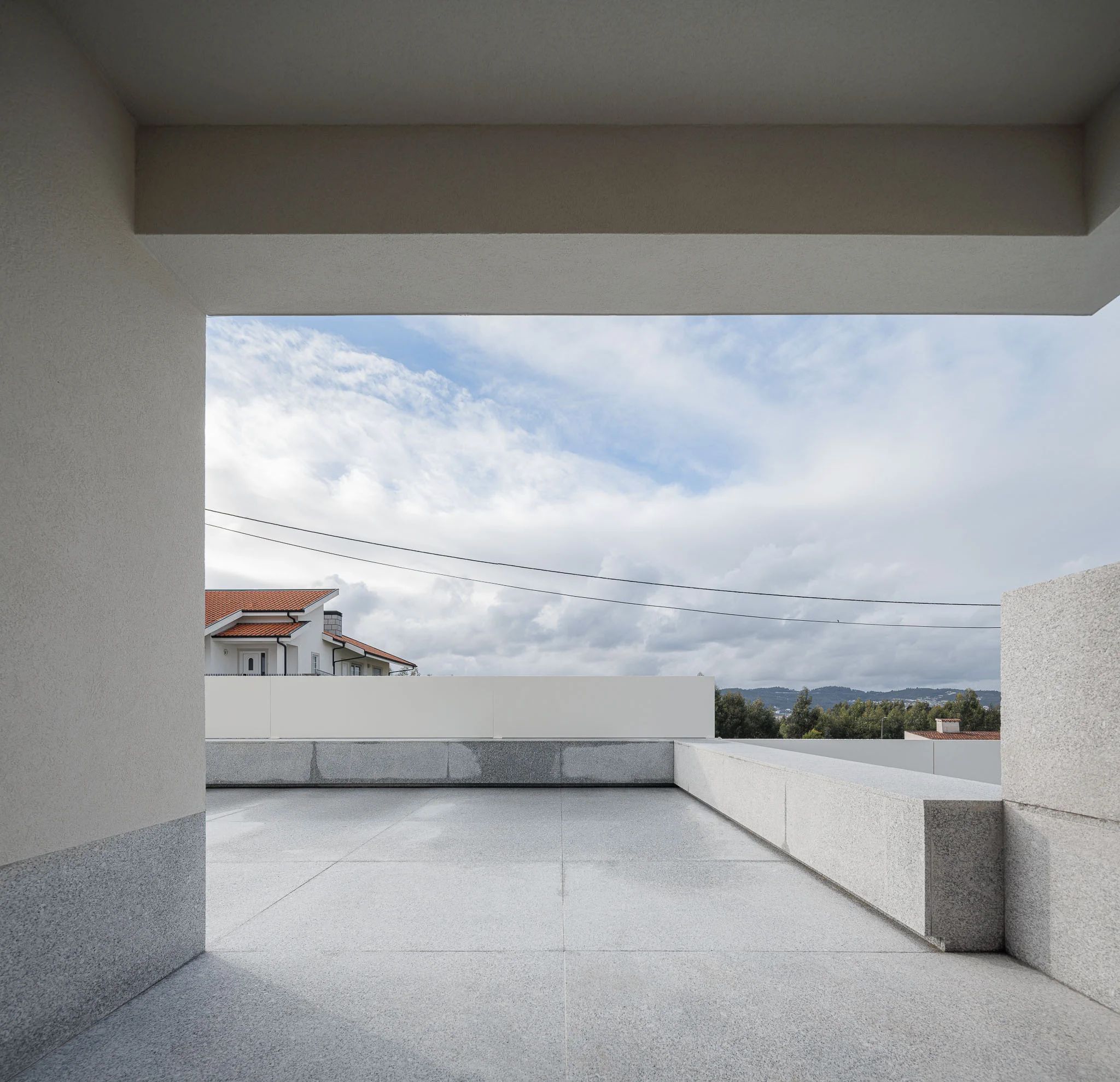 Vista do terraço com pavimento em granito, paredes brancas e paisagem ao fundo. — Casa em Santa Marinha arquitetura Helder da Rocha Arquitectos em Lousada